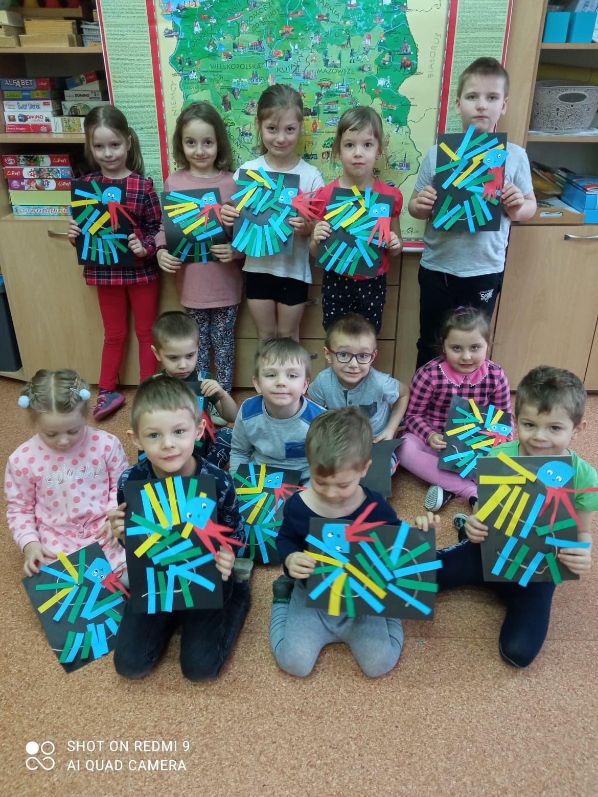 Dzieci przedstawiają swoje prace wykonane z kolorowych pasków umieszczonych na czarnej kartce