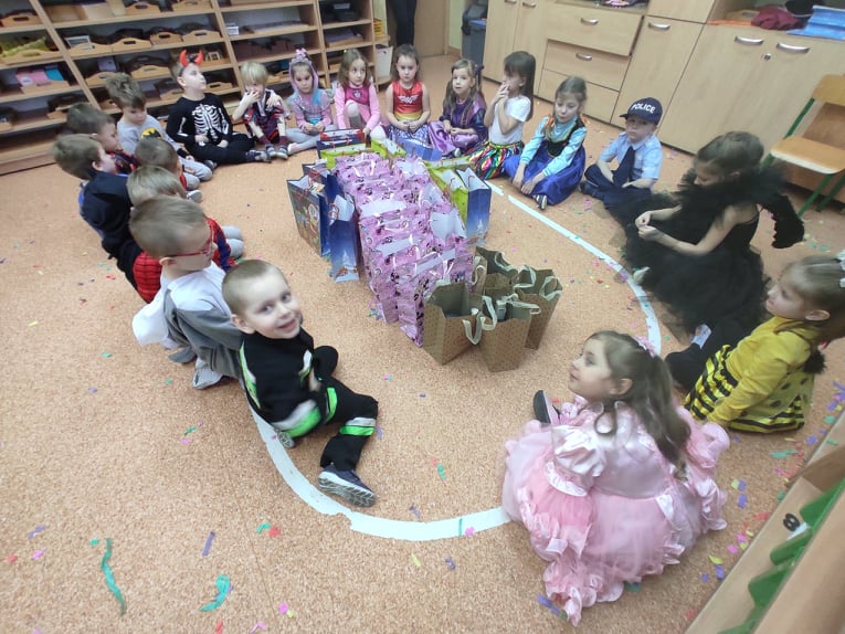 Dzieci z grupy II siedzą w kole (na środku kolorowe prezenty)