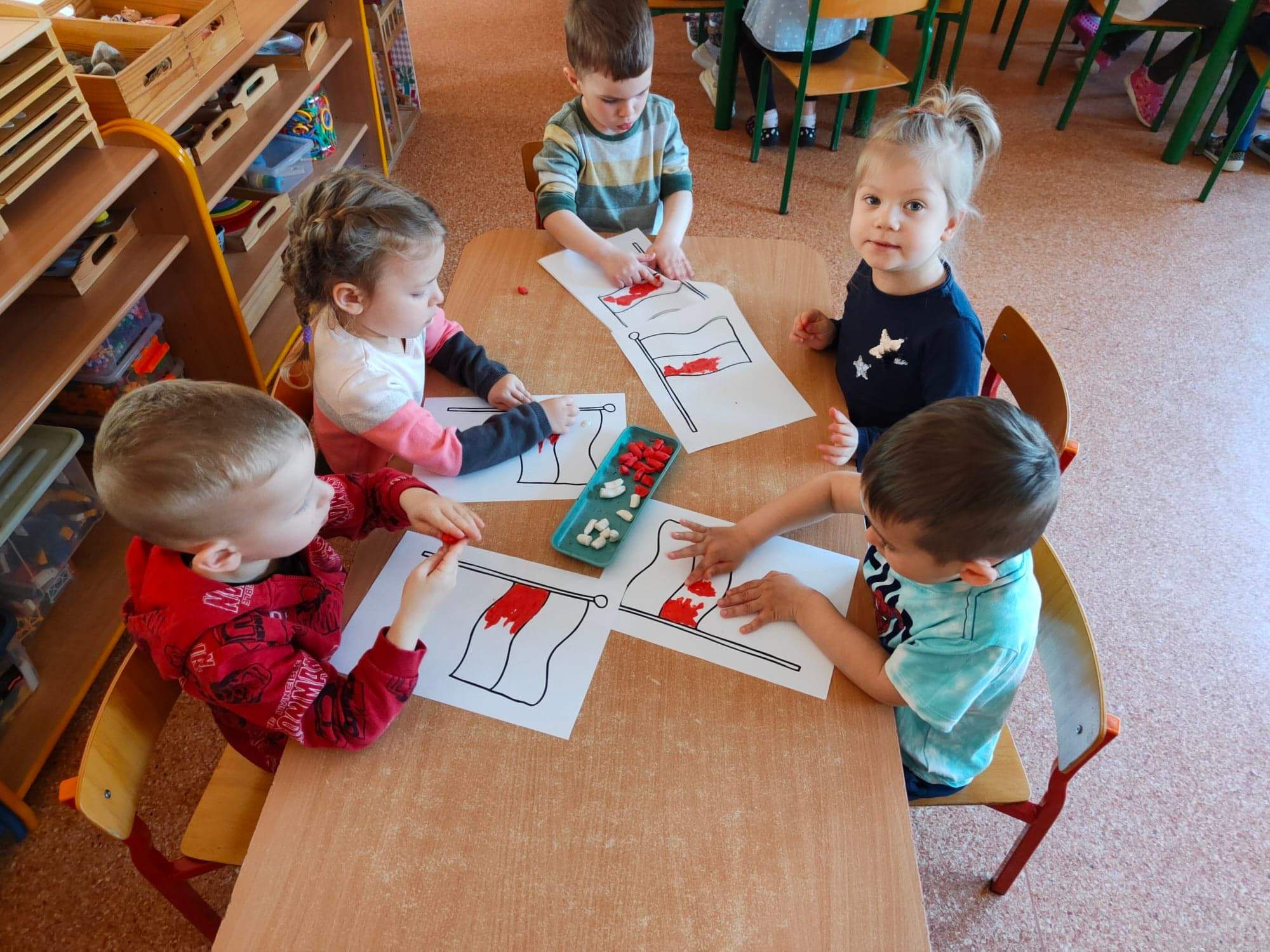 Dzieci wykonują pracę plastyczną - wyklejają plasteliną szablon Flagi Polski.
