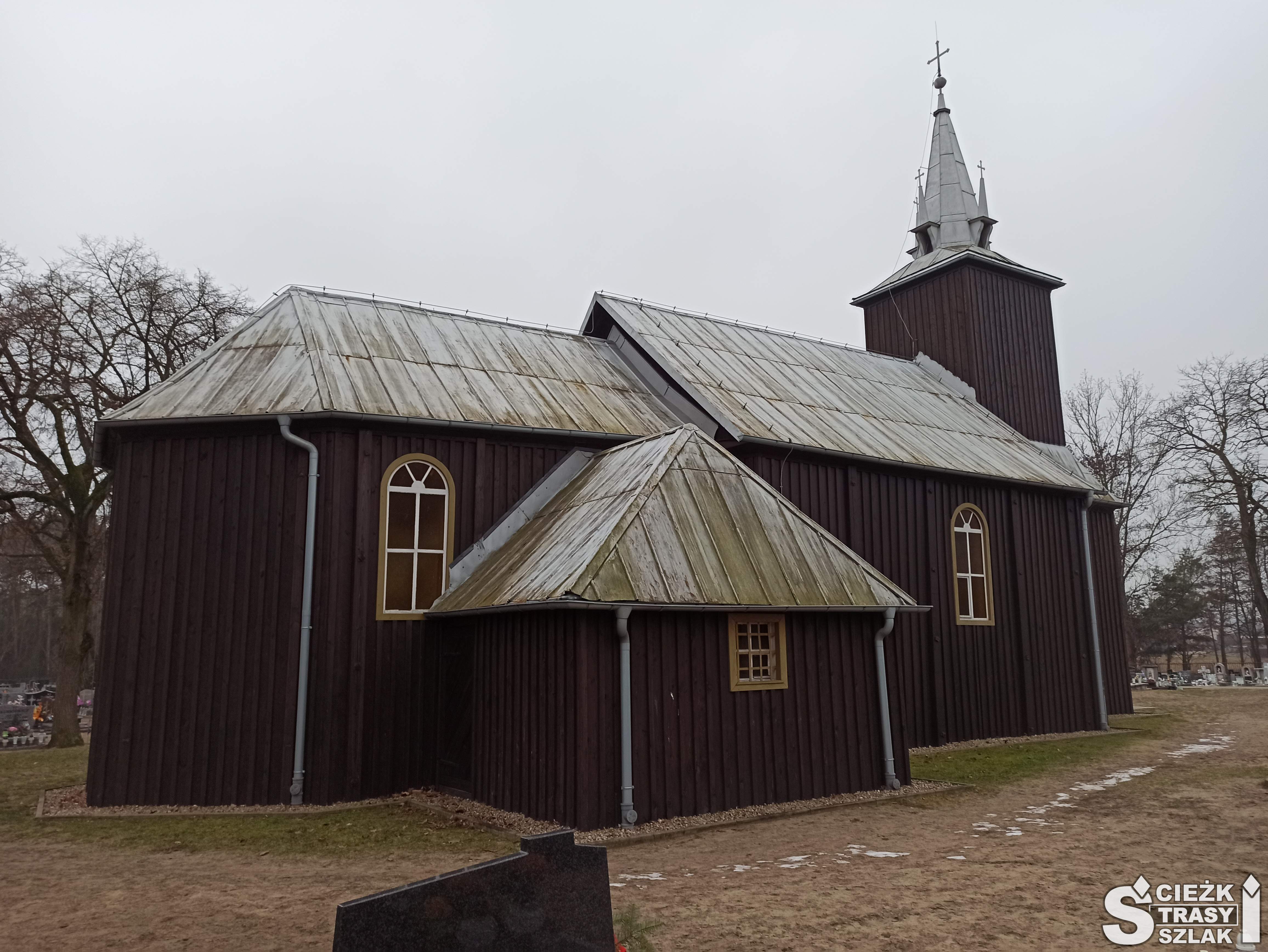 Drewniany kościół w Kębłowie z blaszanym dachem, i wieżą kościelną w brązowym kolorze