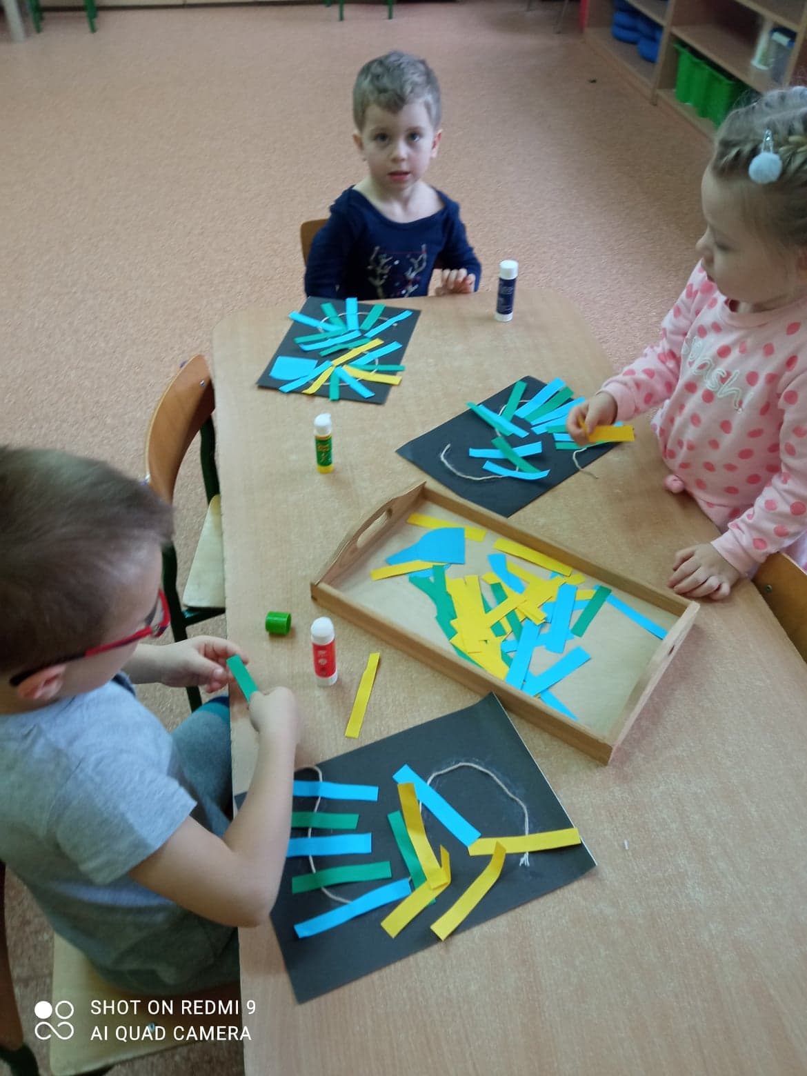 Dzieci z wyciętych kolorowych pasków kleją według wzoru Smoka Wawelskiego