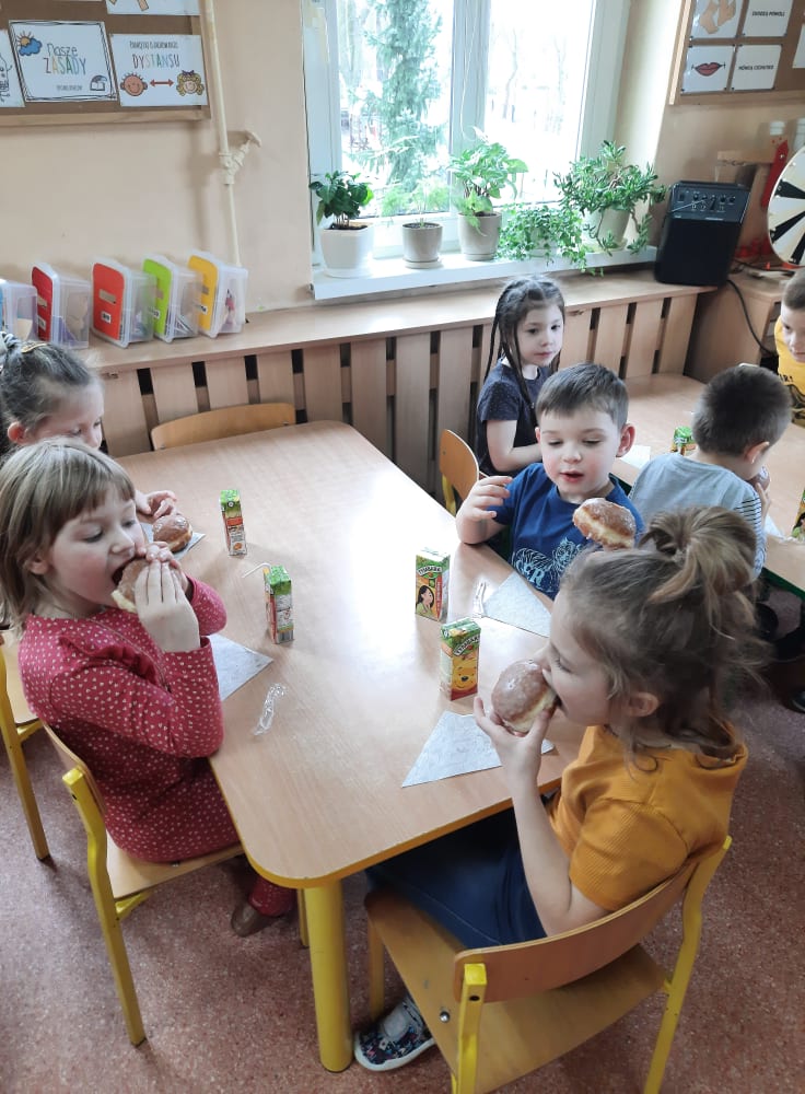 Wspólnie świętujemy Tłusty Czwartek. Dzieci jedzą pyszne pączki z dżemem.