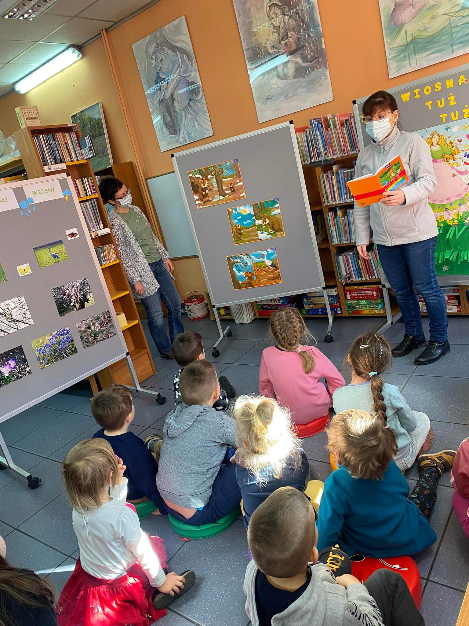 Dzieci uważnie słuchają opowiadania czytanego przez Panią bibliotekarke.