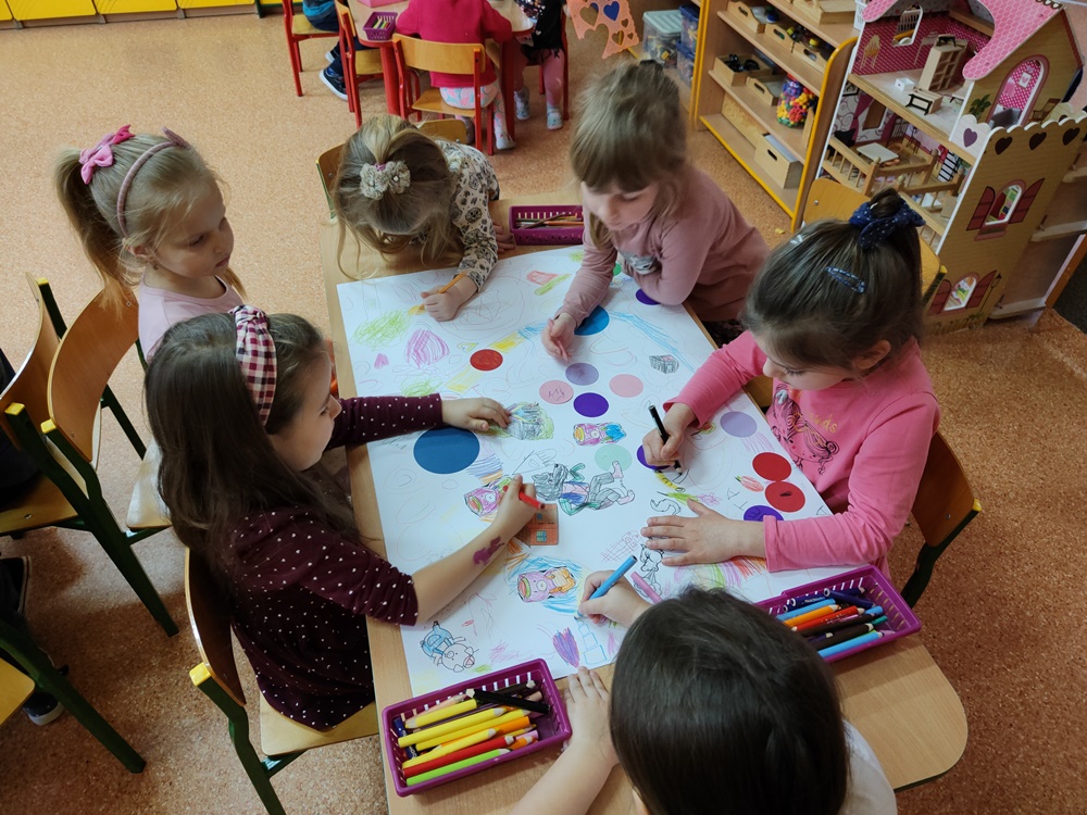 Dzieci wspólnie tworzą bajkową grę ścigankę. Kolorują, przyklejają kolorowe kółeczka.