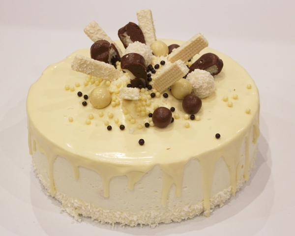 Śmietankowy tort z wiórkami kokosowymi o smaku rumowo-kokosowym oblany białą czekoladą.