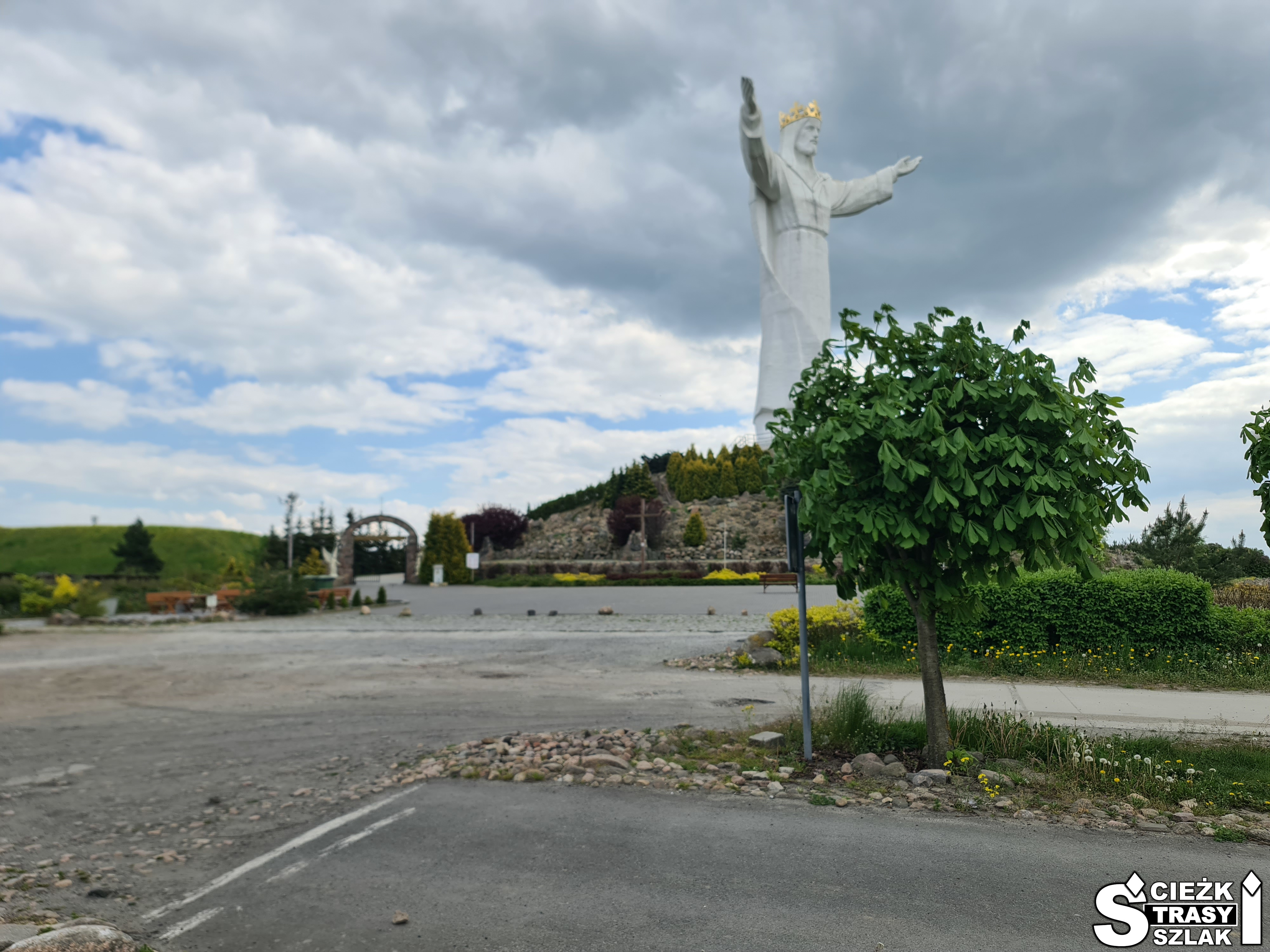 Monumentalny pomnika Chrystusa Króla z rozłożonymi rękami na wzgórzu, do którego prowadzą ścieżki i alejki