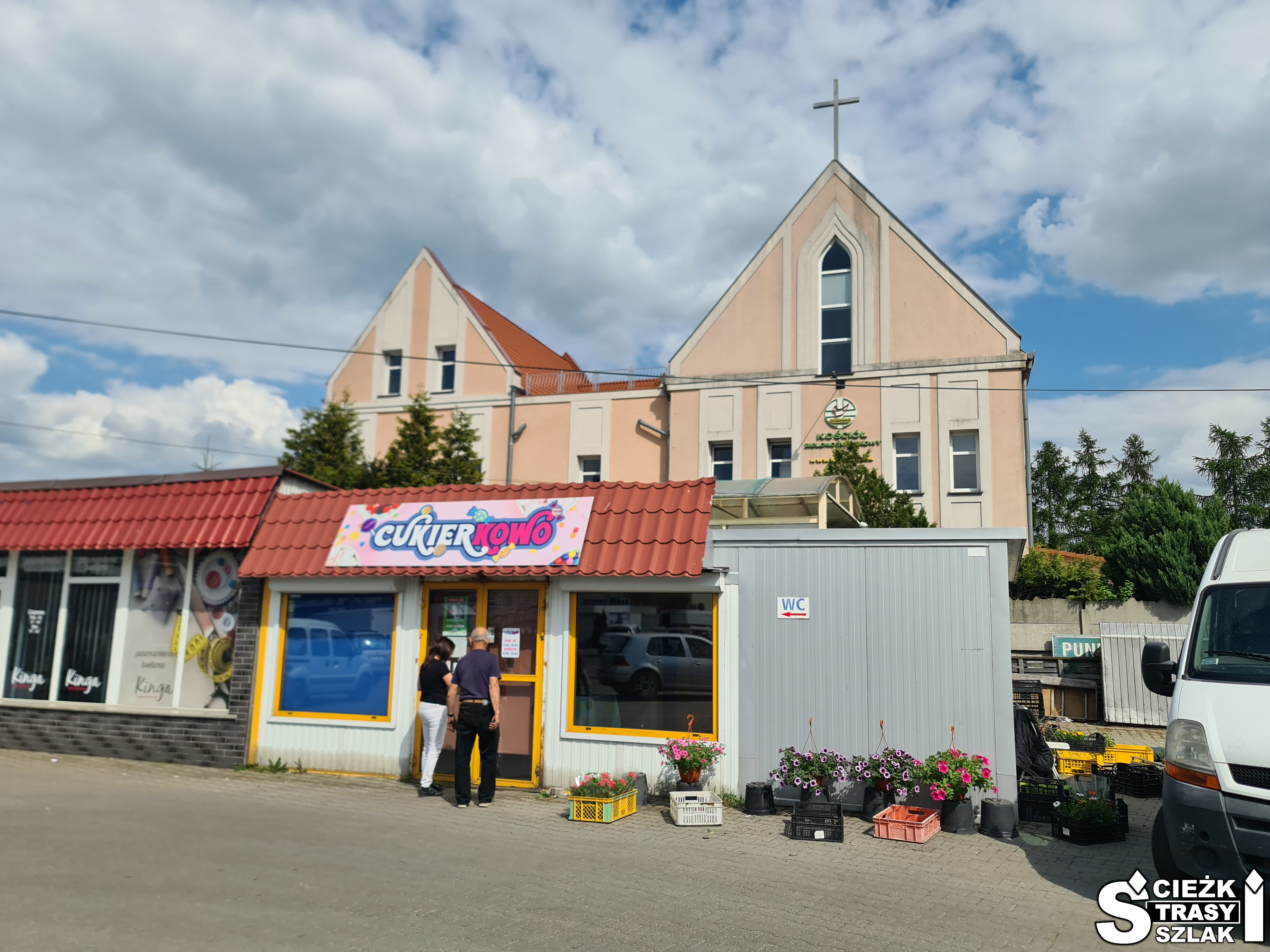 Budynek kościoła zielonoświątkowców w Świebodzinie z kremowo-beżową elewacją i krzyżem na dachu za kioskami ze słodyczami