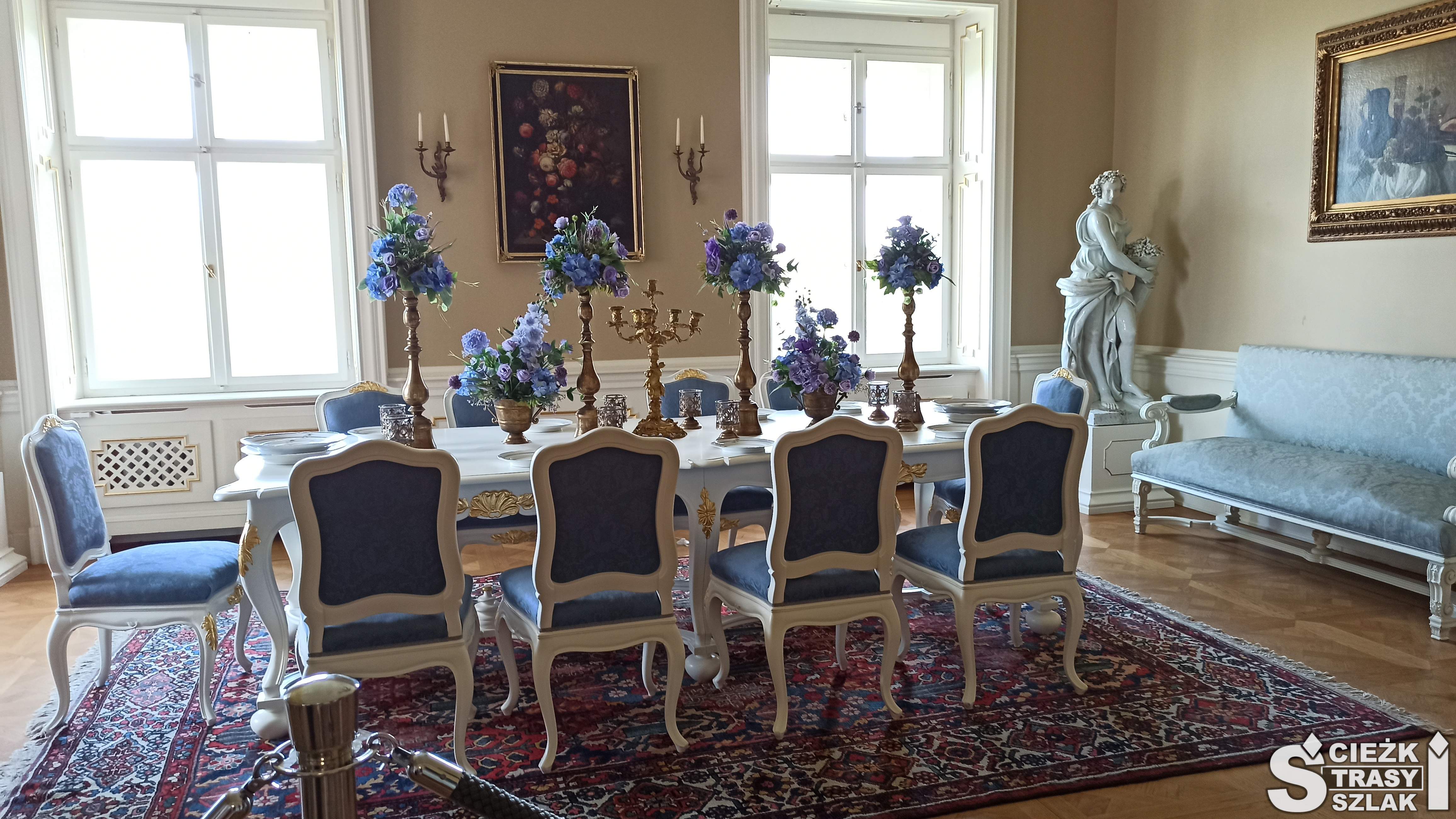 Białe krzesła z niebieską tapicerką wokół stołu w jadalni księżnej Daisy z Zamku Książ