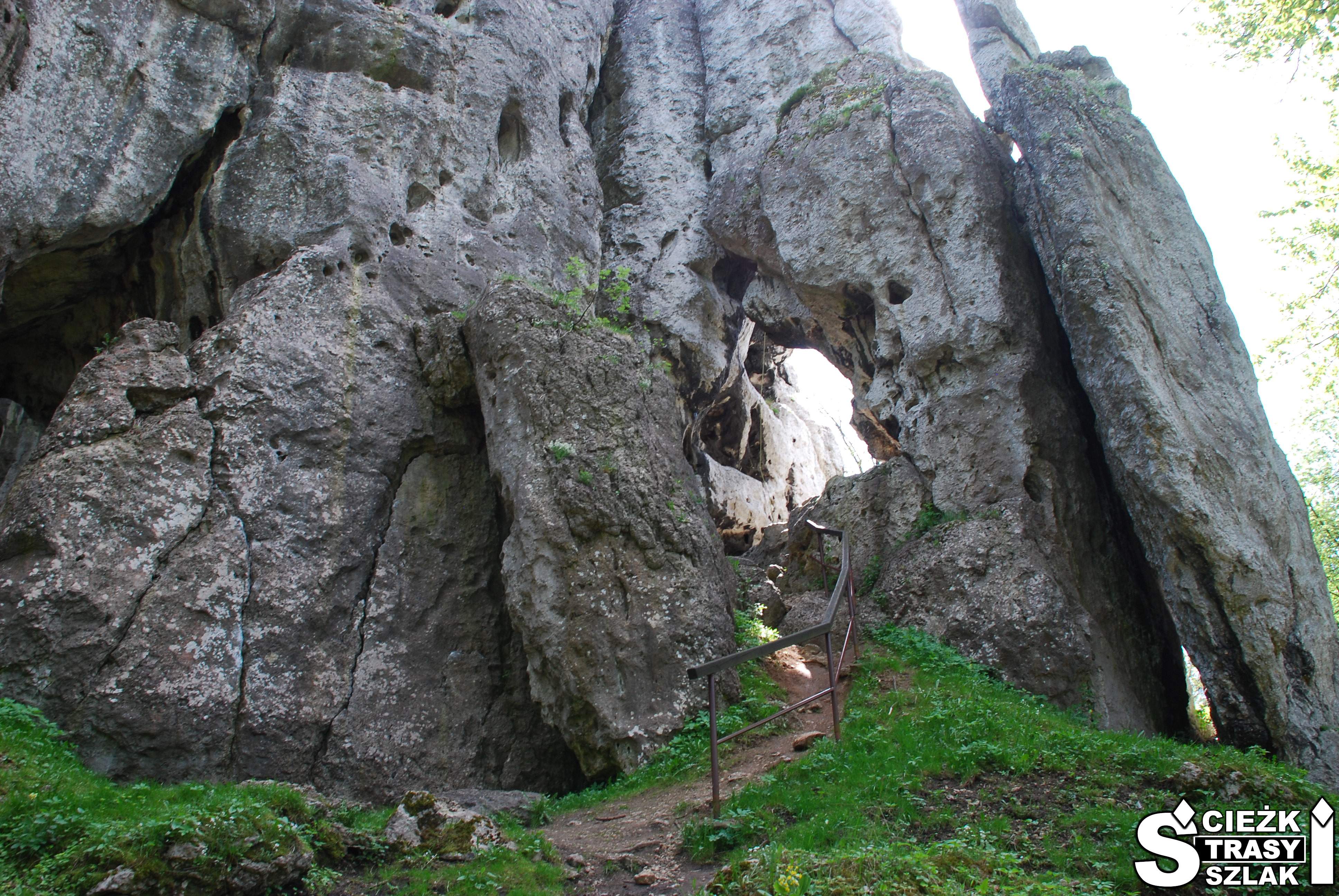 Wąskie, strome schody z metalową barierką do jaskini w skale wapiennej na ścieżce dydaktycznej do Grodu Birów w Podzamczu
