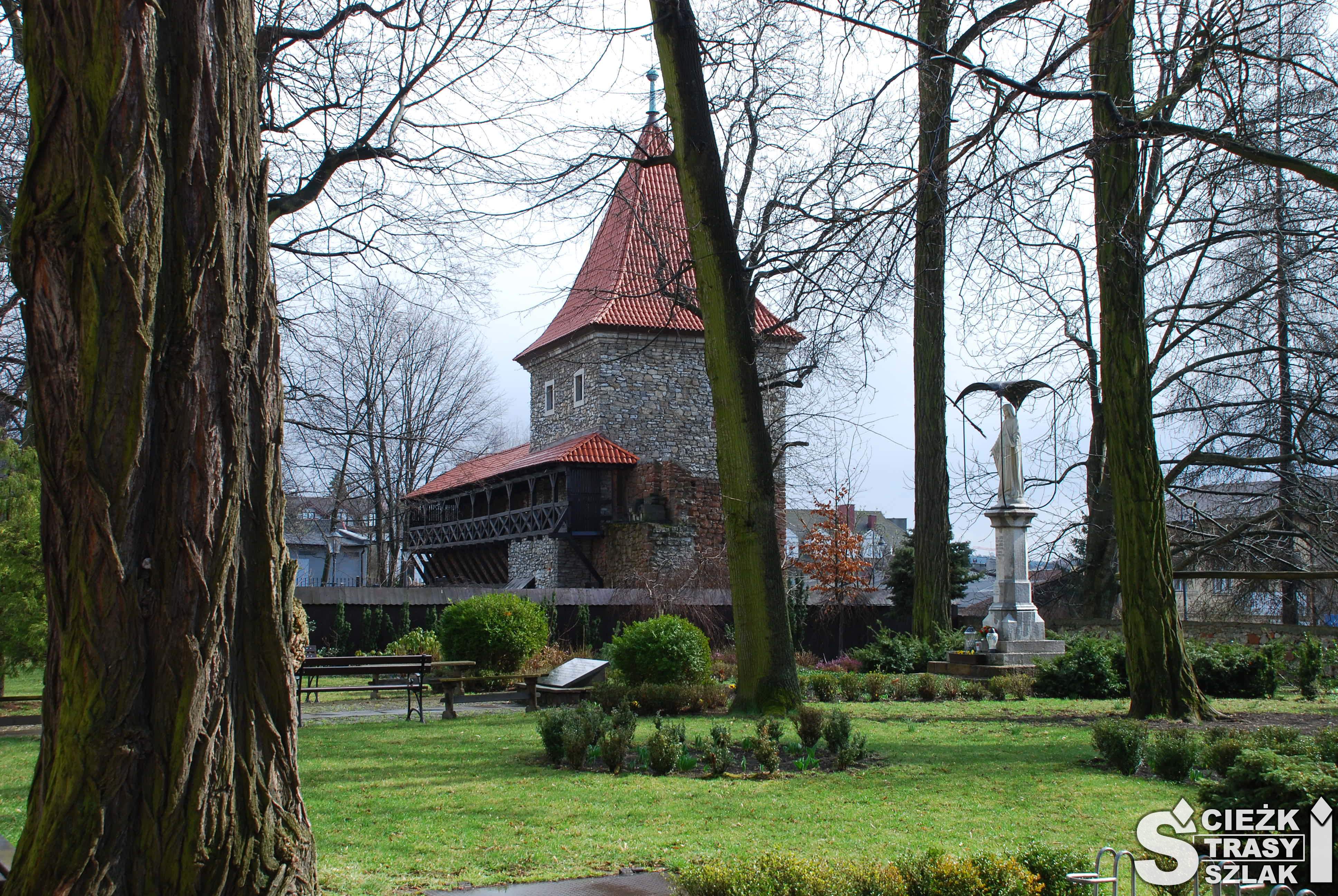 Zabytkowa baszta w Olkuszu za drzewami i figurą Matki Boskiej w parku koło Bazyliki Św. Andrzeja
