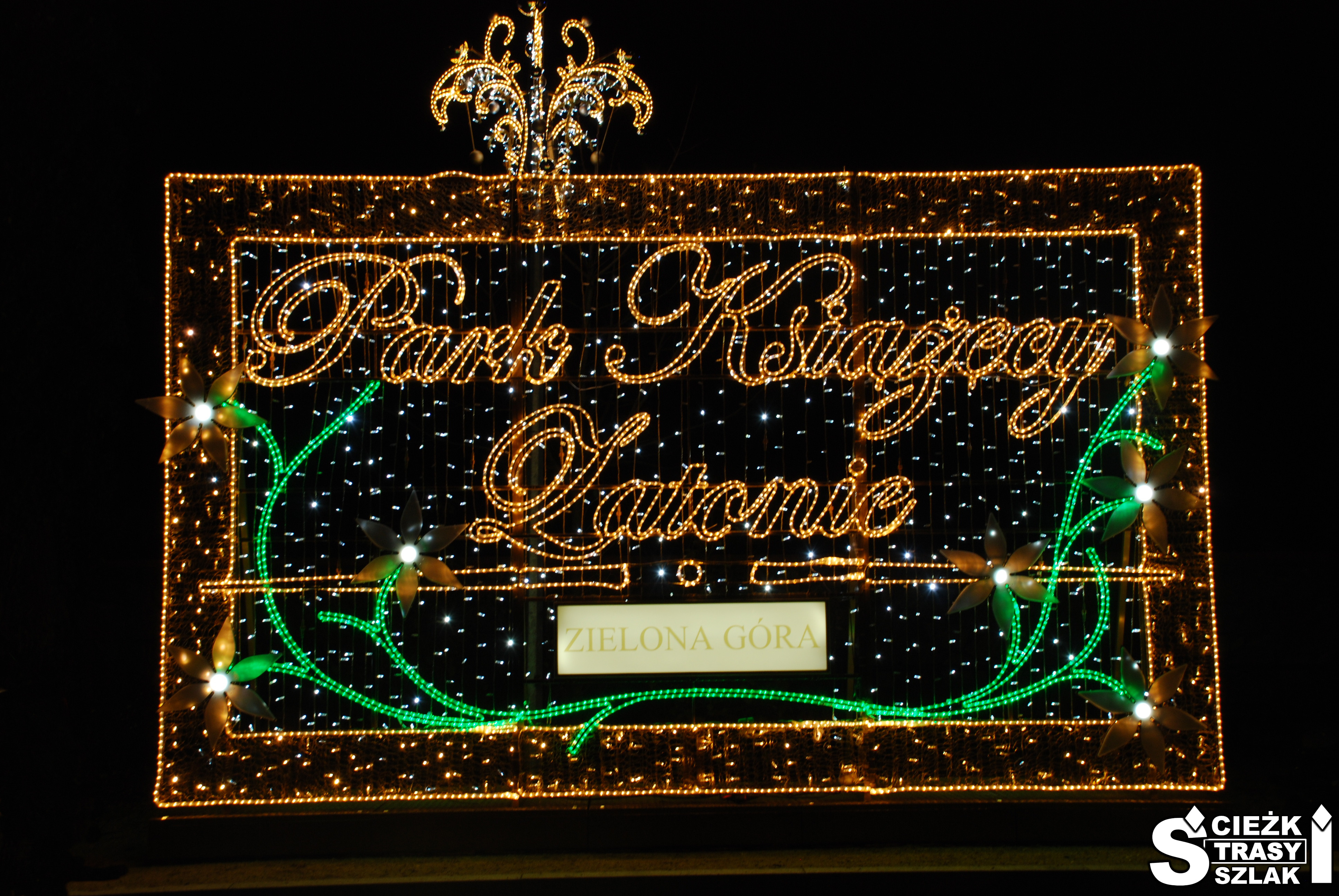 Podświetlony na pomarańczowo napis Pałac Książęcy Zatonie Zielona Góra przy wejściu do Parku Światła
