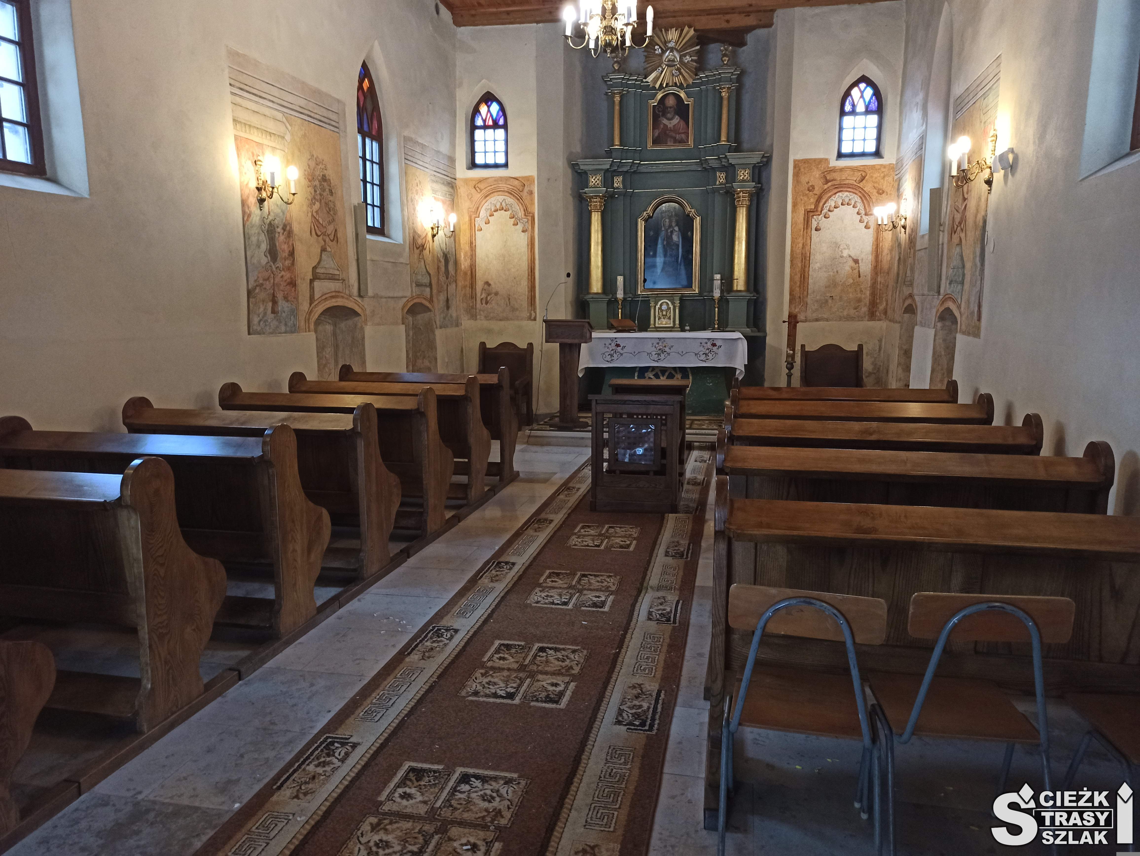 Drewniany ołtarz otoczony pierwotną polichromią w kaplicy cmentarnej w Bydlinie z ławkami
