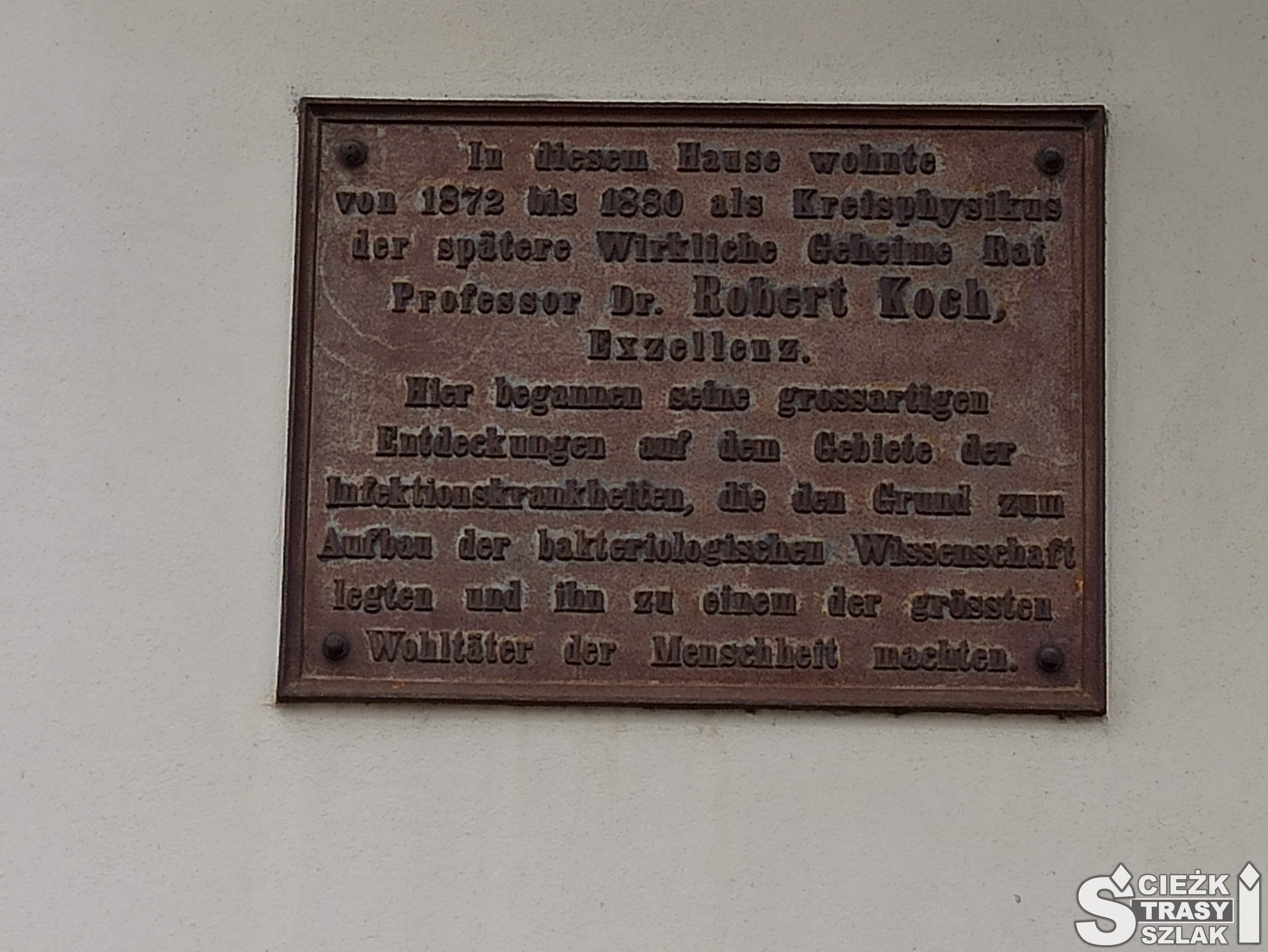 Kwadratowa tablica pamiątkowa z brązu z dedykacją w języku niemieckim przy wejściu do Muzeum Kocha