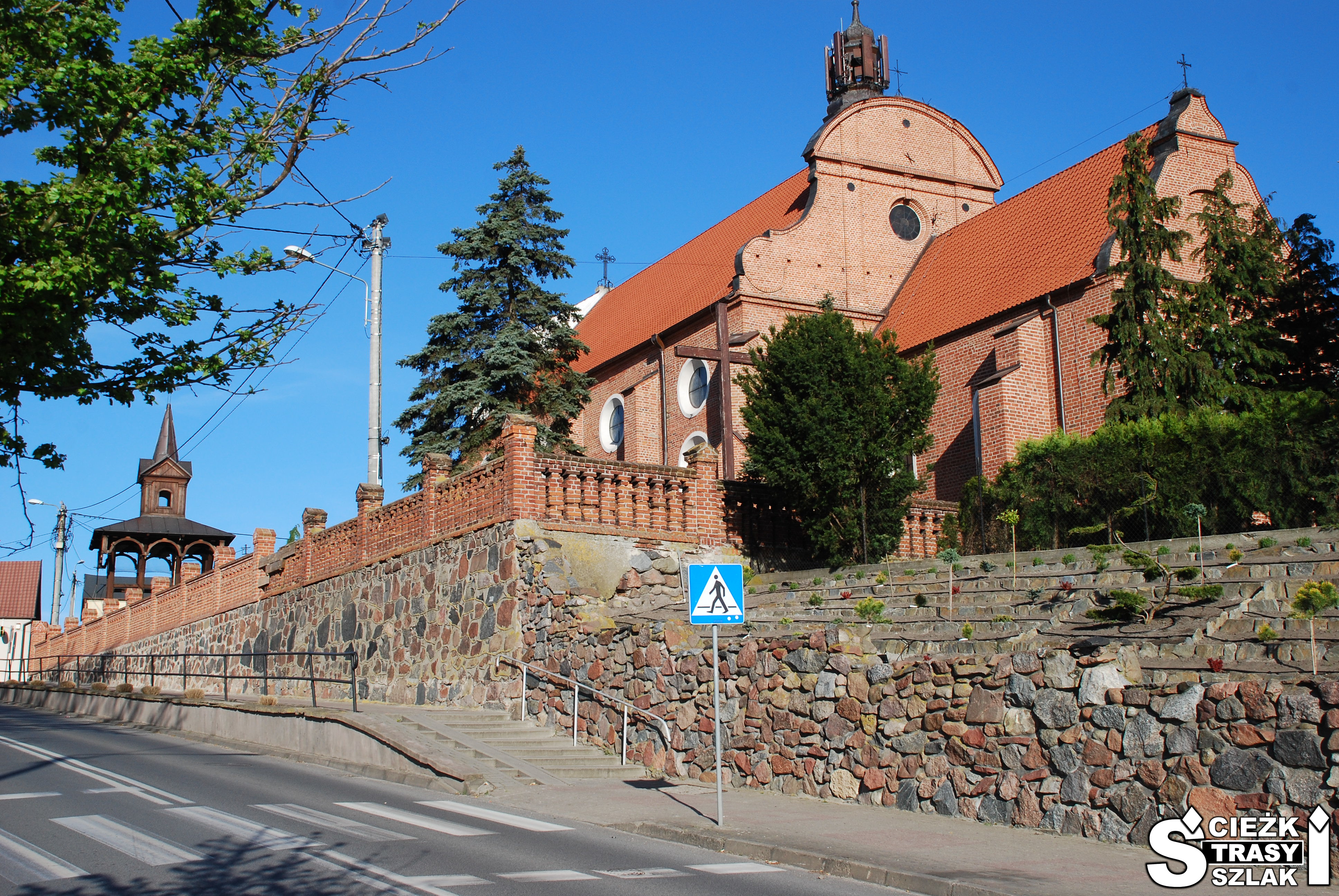 Zabytkowy kościół z czerwonej cegły za kamiennym murem klasztoru o.o. franciszkanów z dzwonnicą wolnostojącą przy murze
