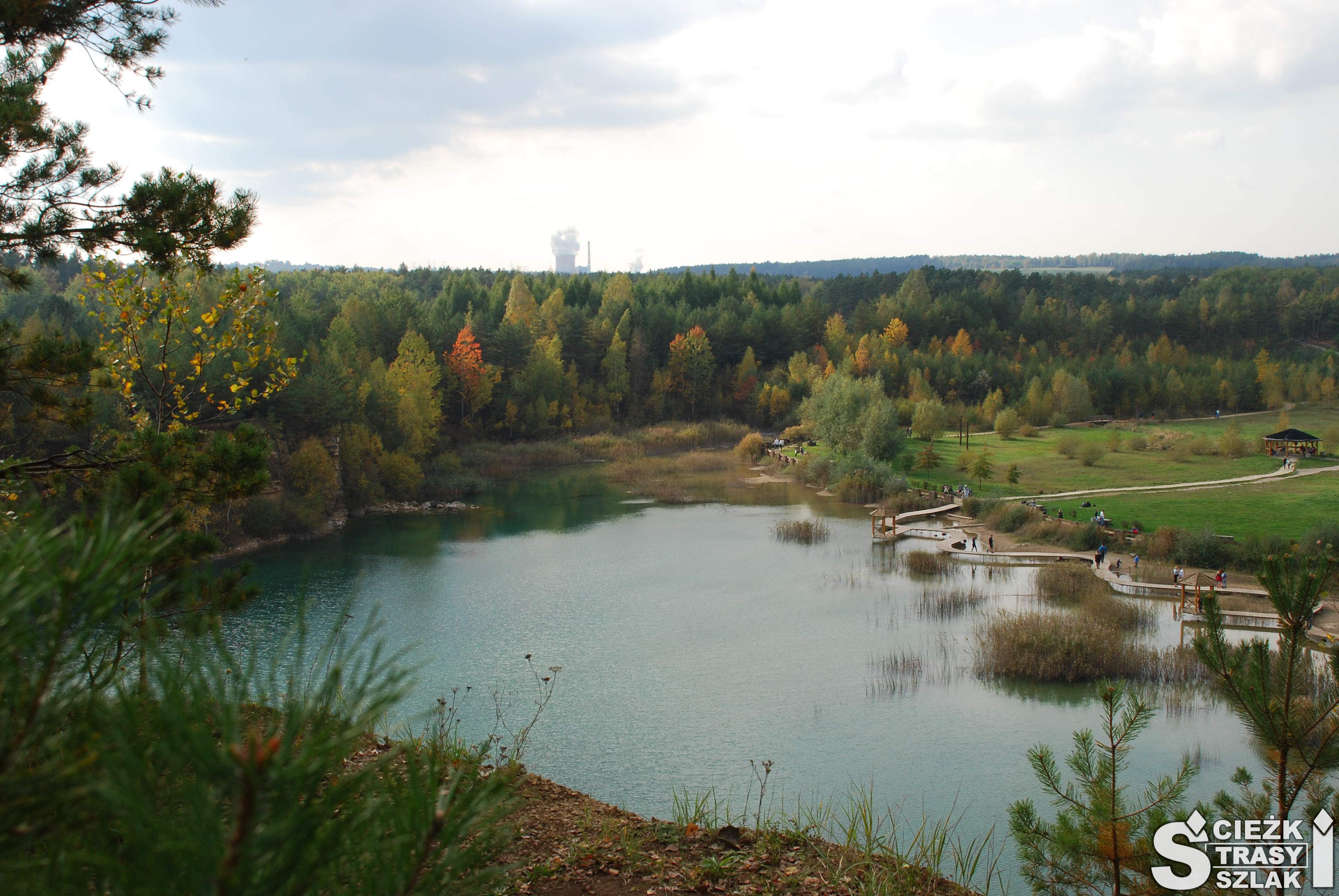 Turkusowe jezioro otoczone drzewami w jesiennej barwie, zielonymi łąkami i skarpami po kamieniołomie w Parku Gródek