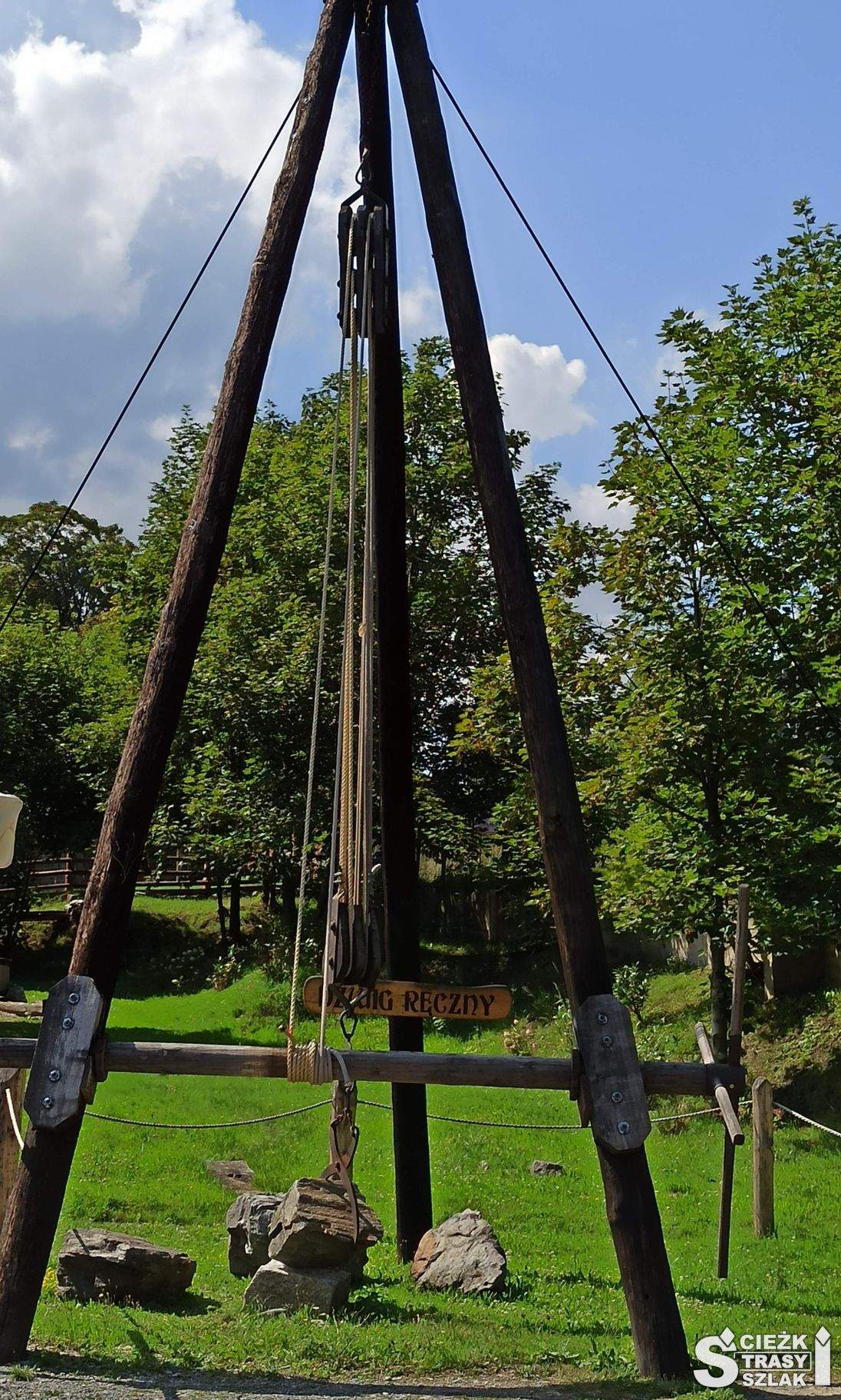 Wysoki dźwig ręczny zbudowany z trzech drewnianych belek tworzących stożek