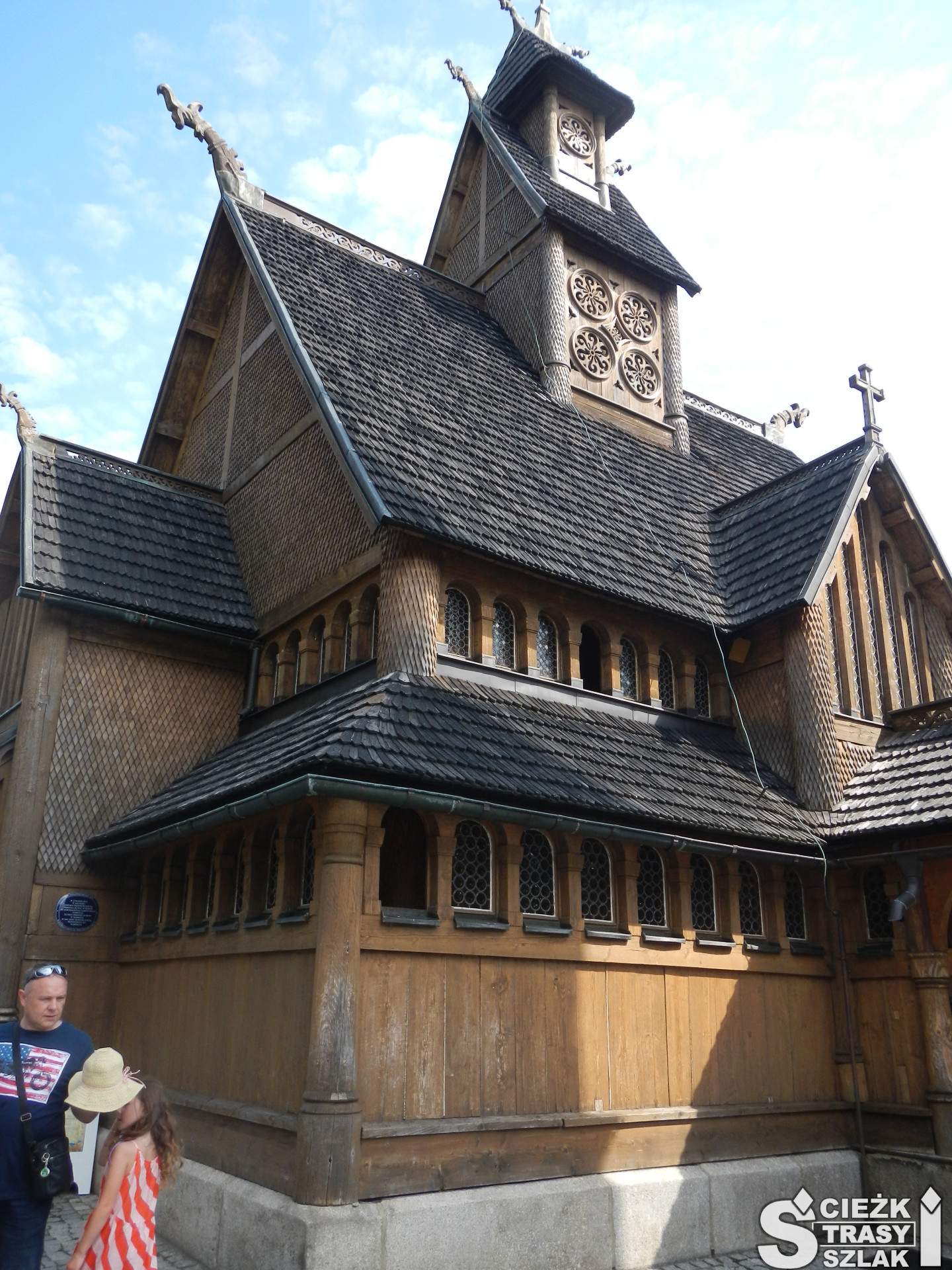 Drewniany kościół z wieżą w stylu zakopiańskim otoczony krużgankiem z witrażami