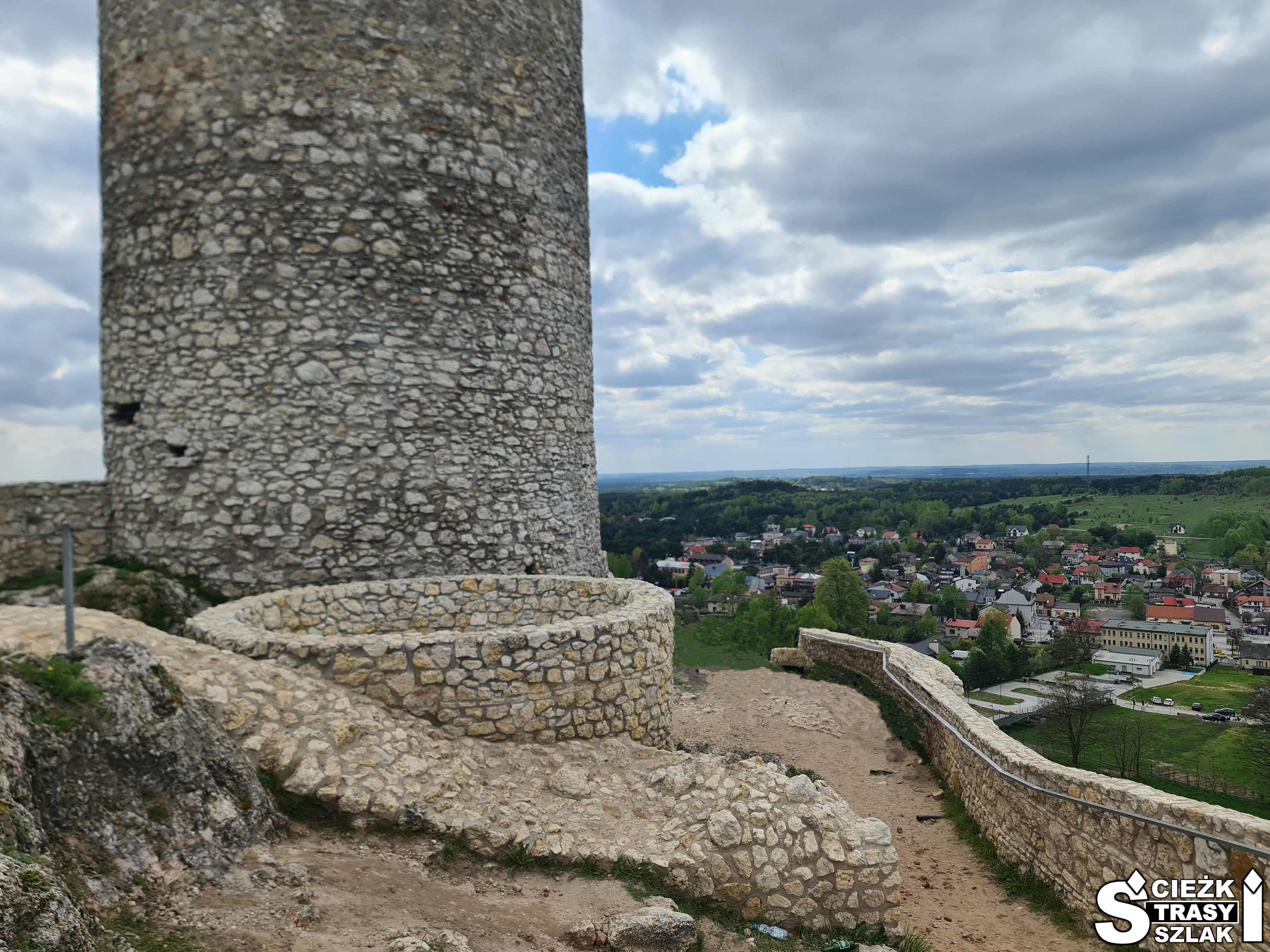 Niski murek z kamienia i cylindryczna wieża Zamku w Olsztynie z panoramą miasta w oddali z punktu widokowego