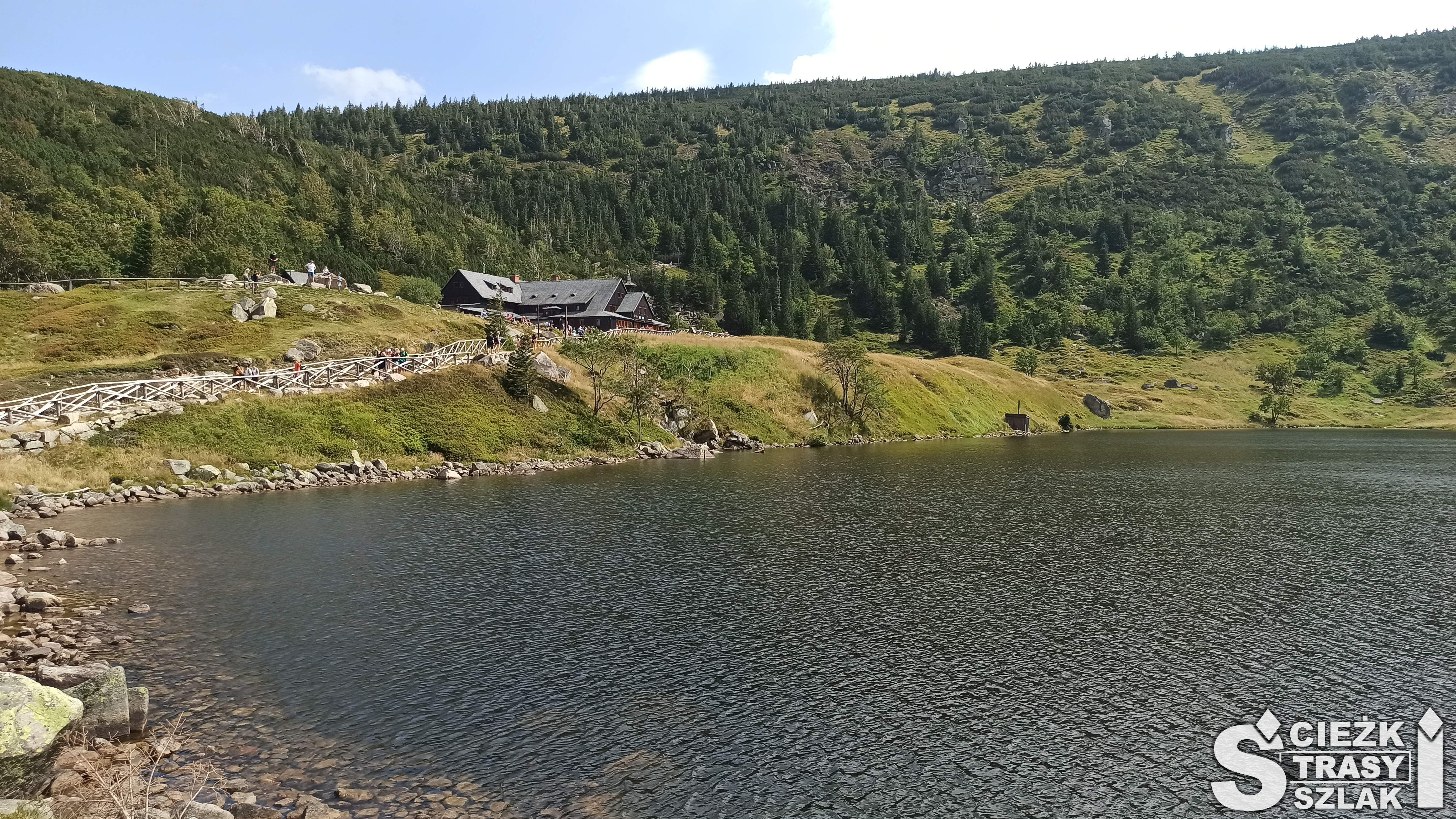 Schronisko Samotnia przy górskim jeziorze Mały Staw położonym z widokiem na góry pokryte zielenią