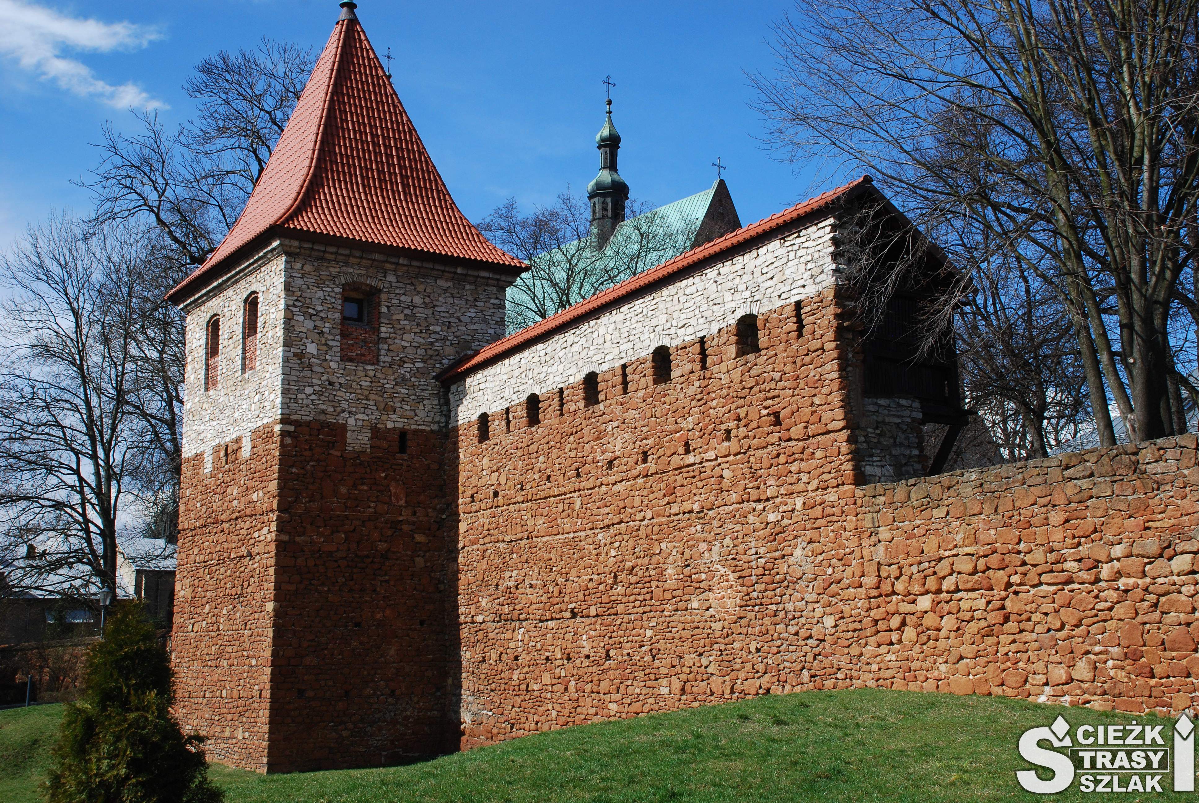 Zabytkowa baszta z czerwonej cegły z podwyższoną wieżą pokrytą dachem i oknami w murze obronnym otaczającym Olkusz