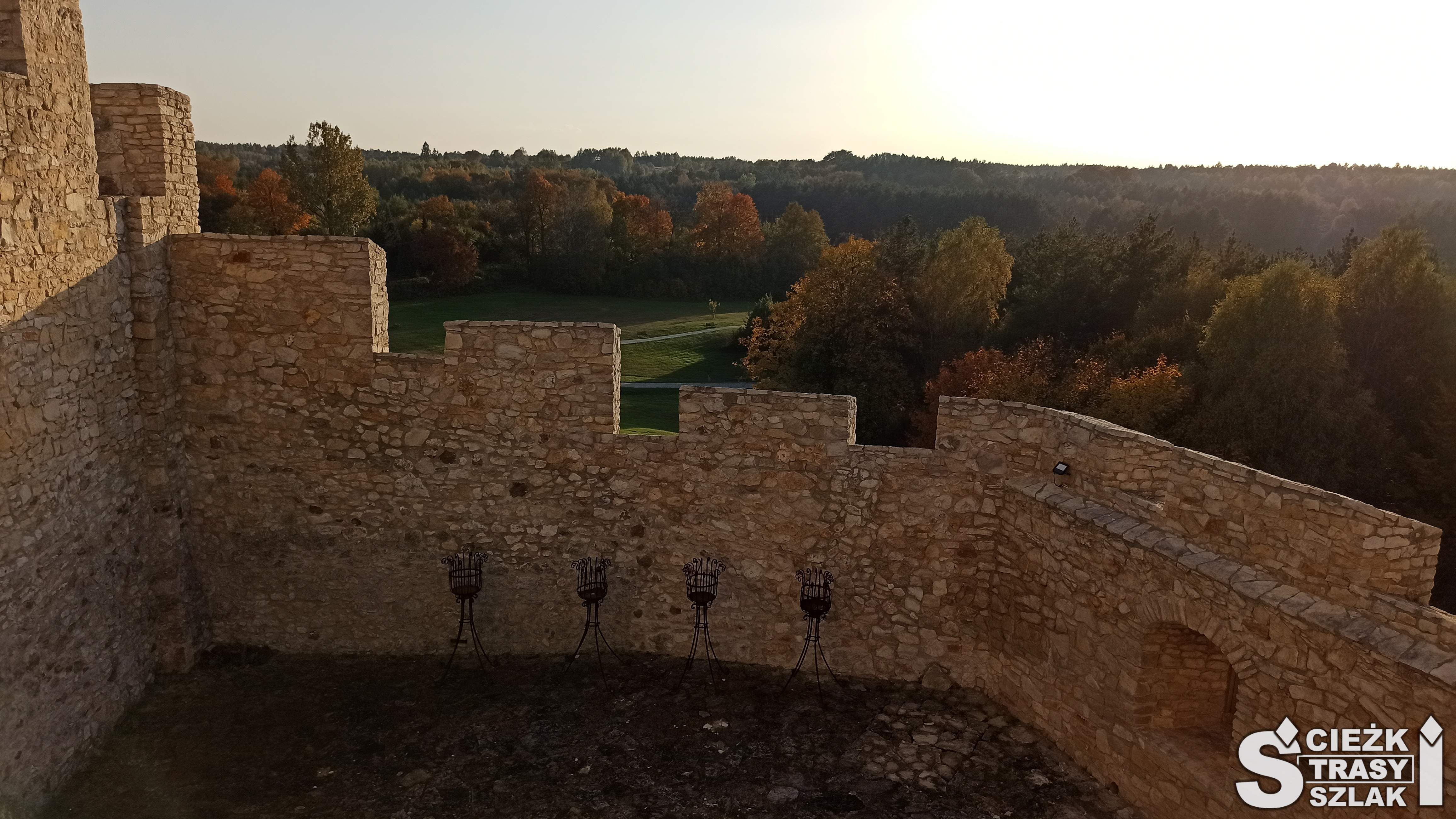 Wysoki mur obronny z kamienia otaczający Zamek Bobolice na tle drzew dotkniętych przez Polską Jesień