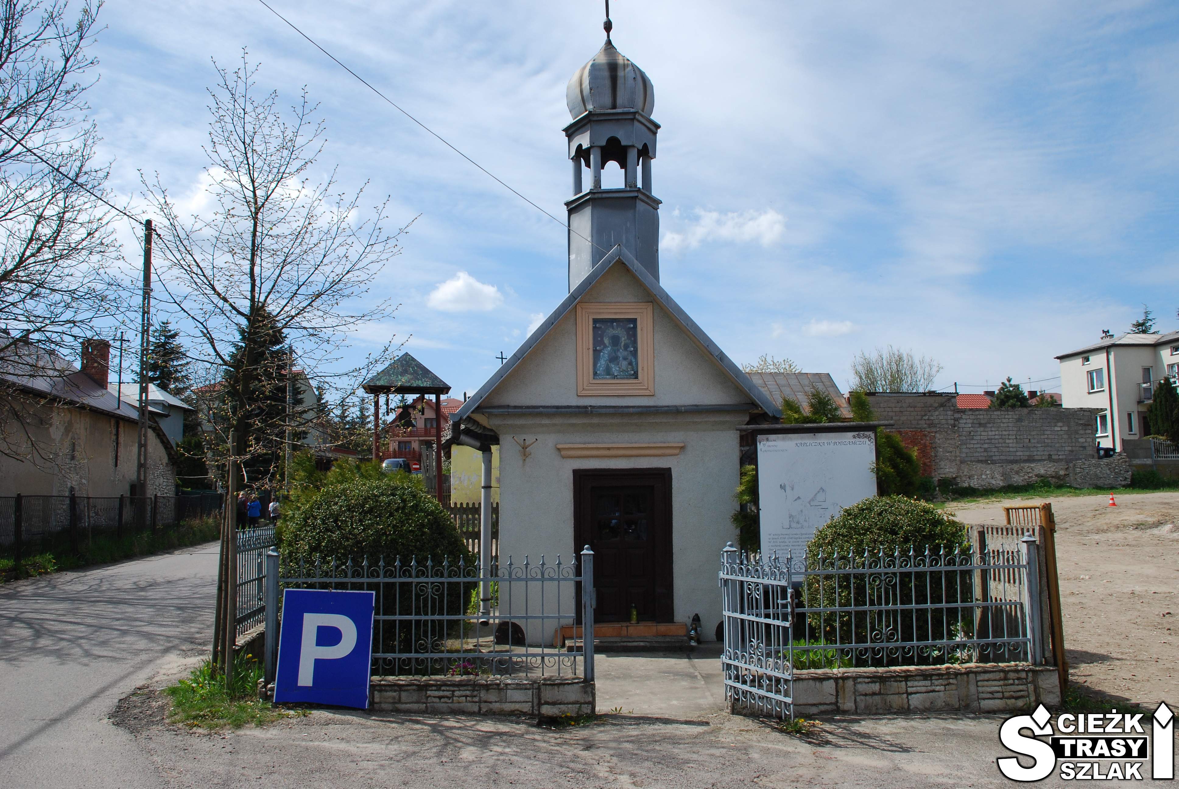 Mała kapliczka w wysoką wieżą za ogrodzeniem i wolnostojącą dzwonnicą przy parkingu Zamku Ogrodzieniec