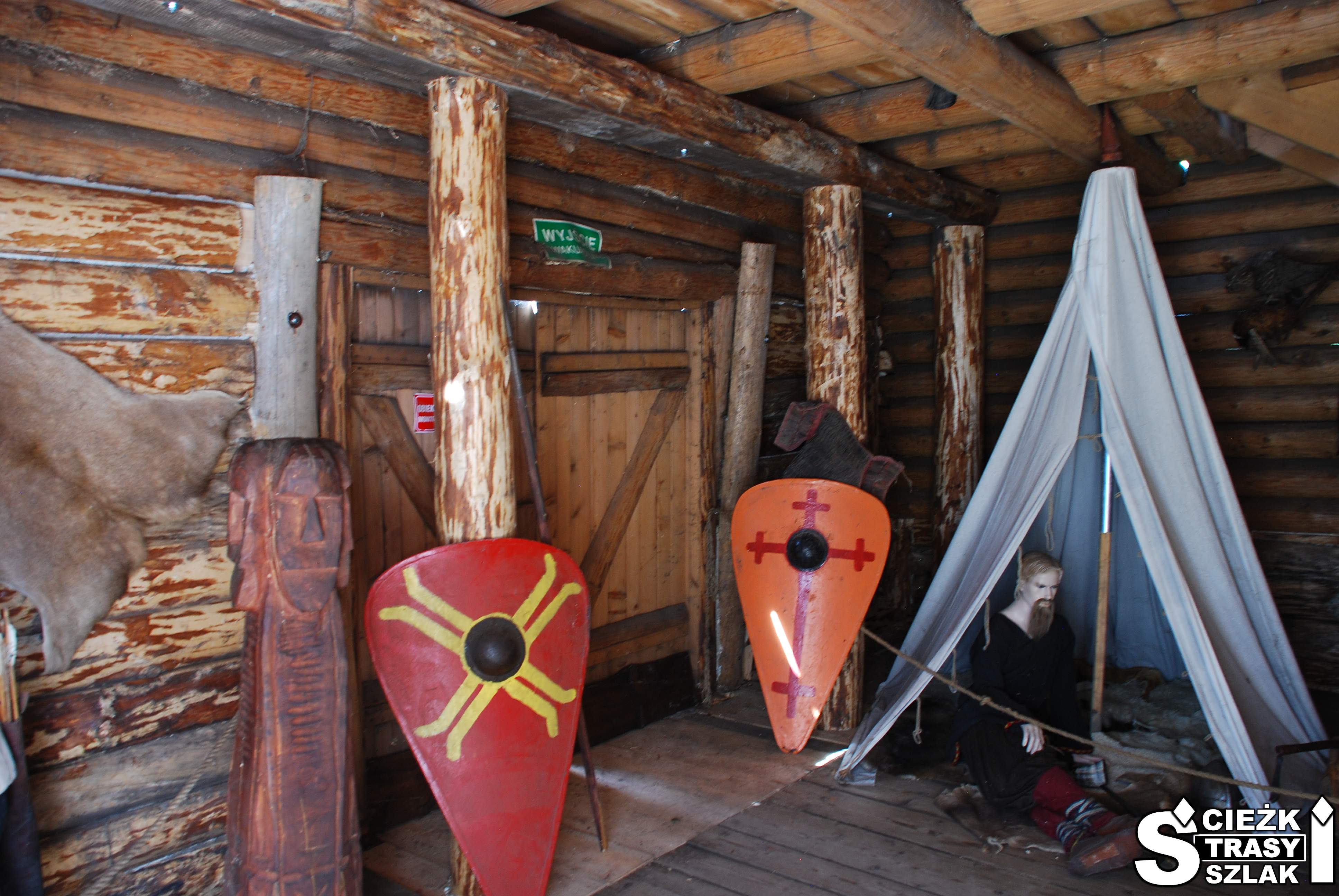 Tarcze z rycerskimi herbami przy namiocie Słowian wewnątrz drewnianej chaty w Grodzie Birów w Podzamczu