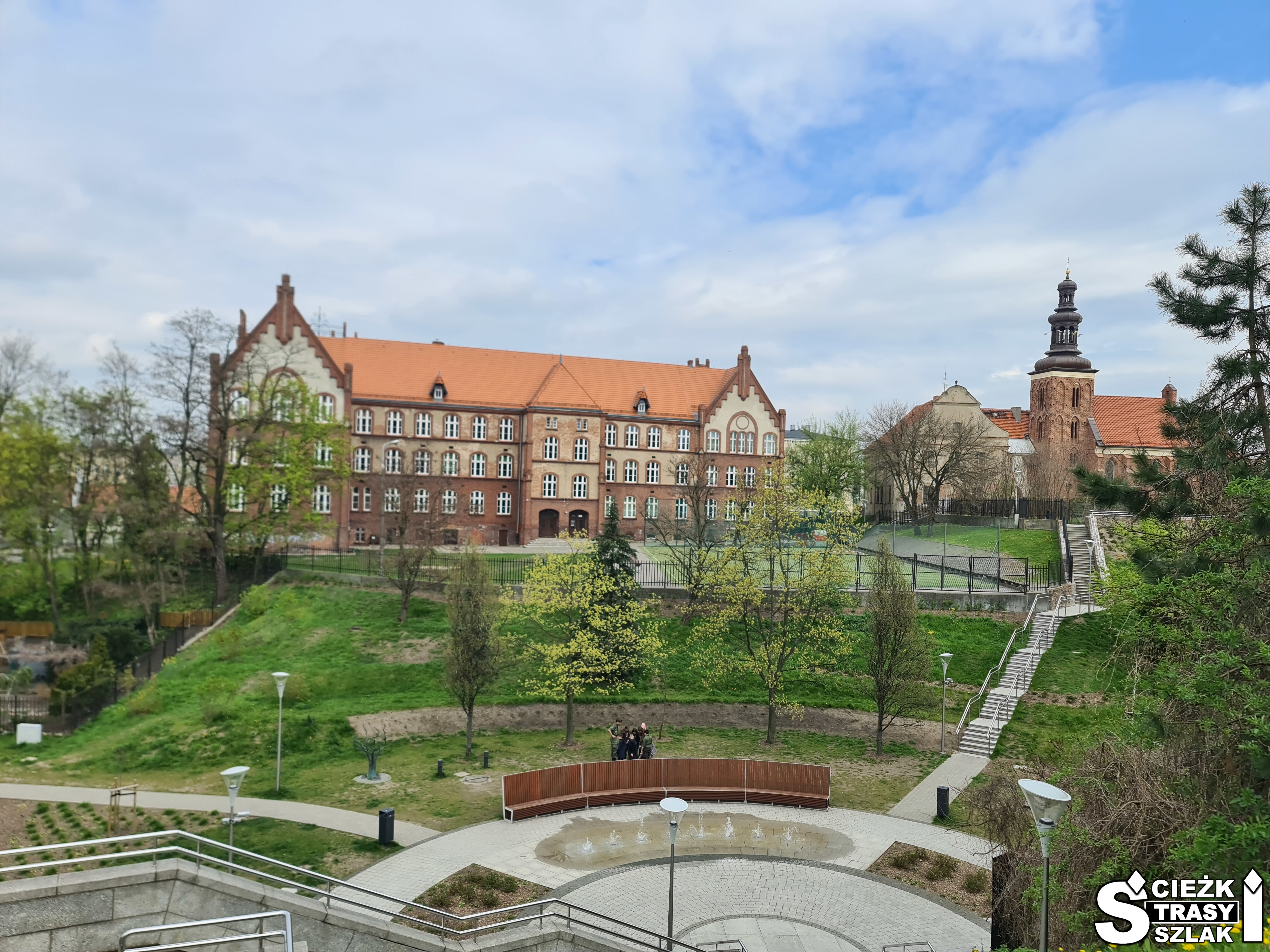 Park miejski ze skateparkiem i fontanną w Dolinie Pojednania w Gnieźnie na tle Klasztoru Franciszkanów