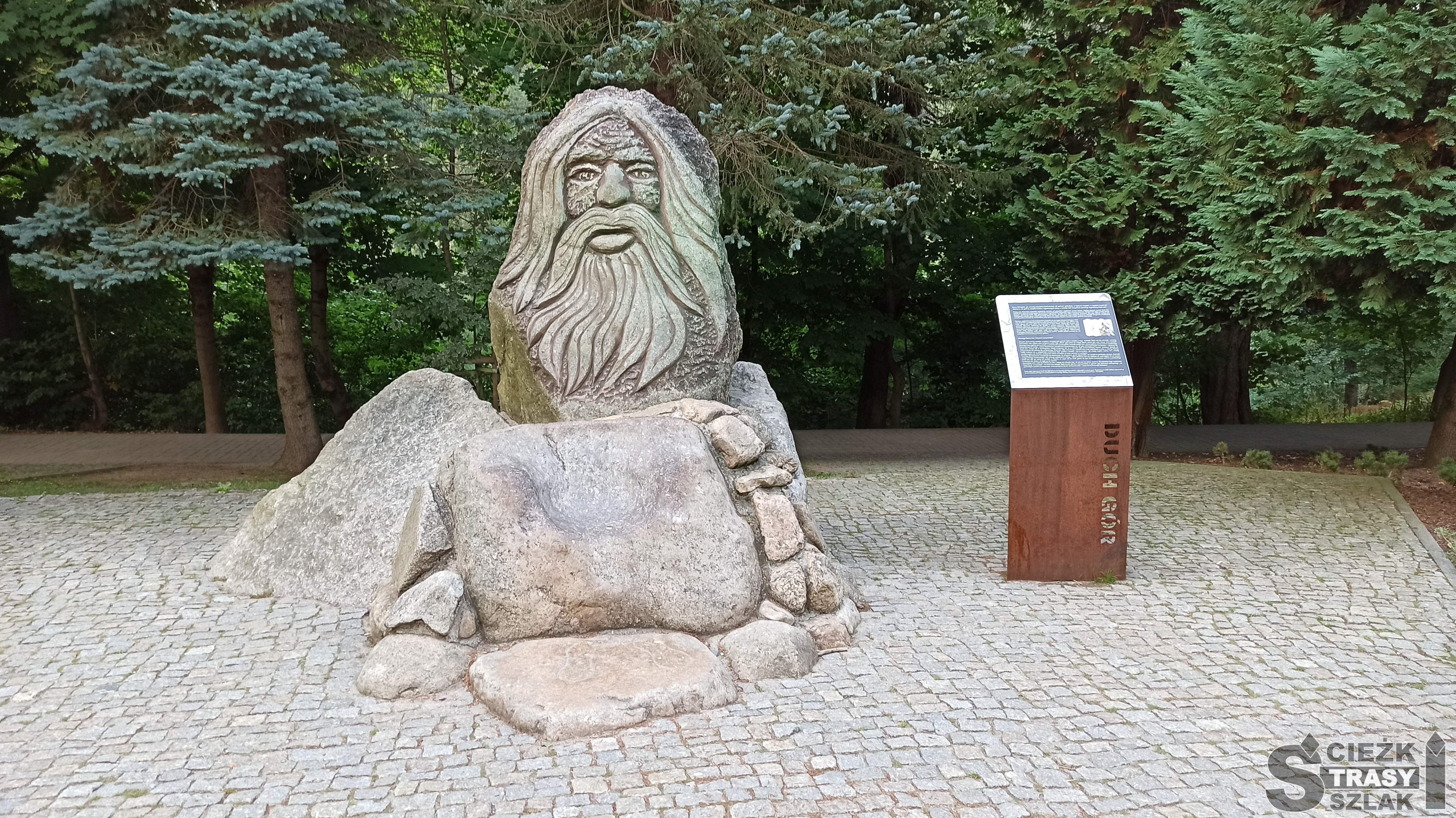 Wysoki kamienny pomnik przypominający postać Ducha Gór postawiony w parku miejsckim w Karpaczu