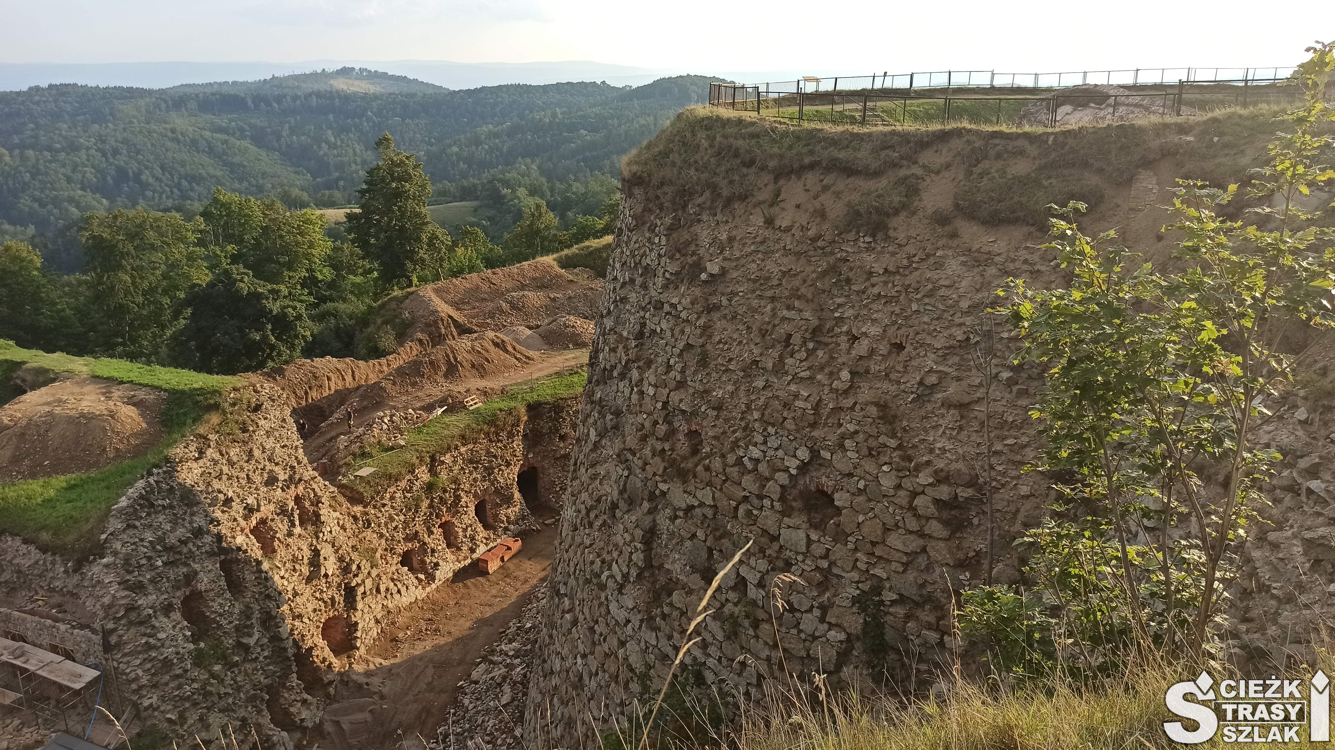 Wysokie skarpy i kamienne mury tworzące bastiony i fortyfikacje Twierdzy Srebrna Góra ponad koronami drzew