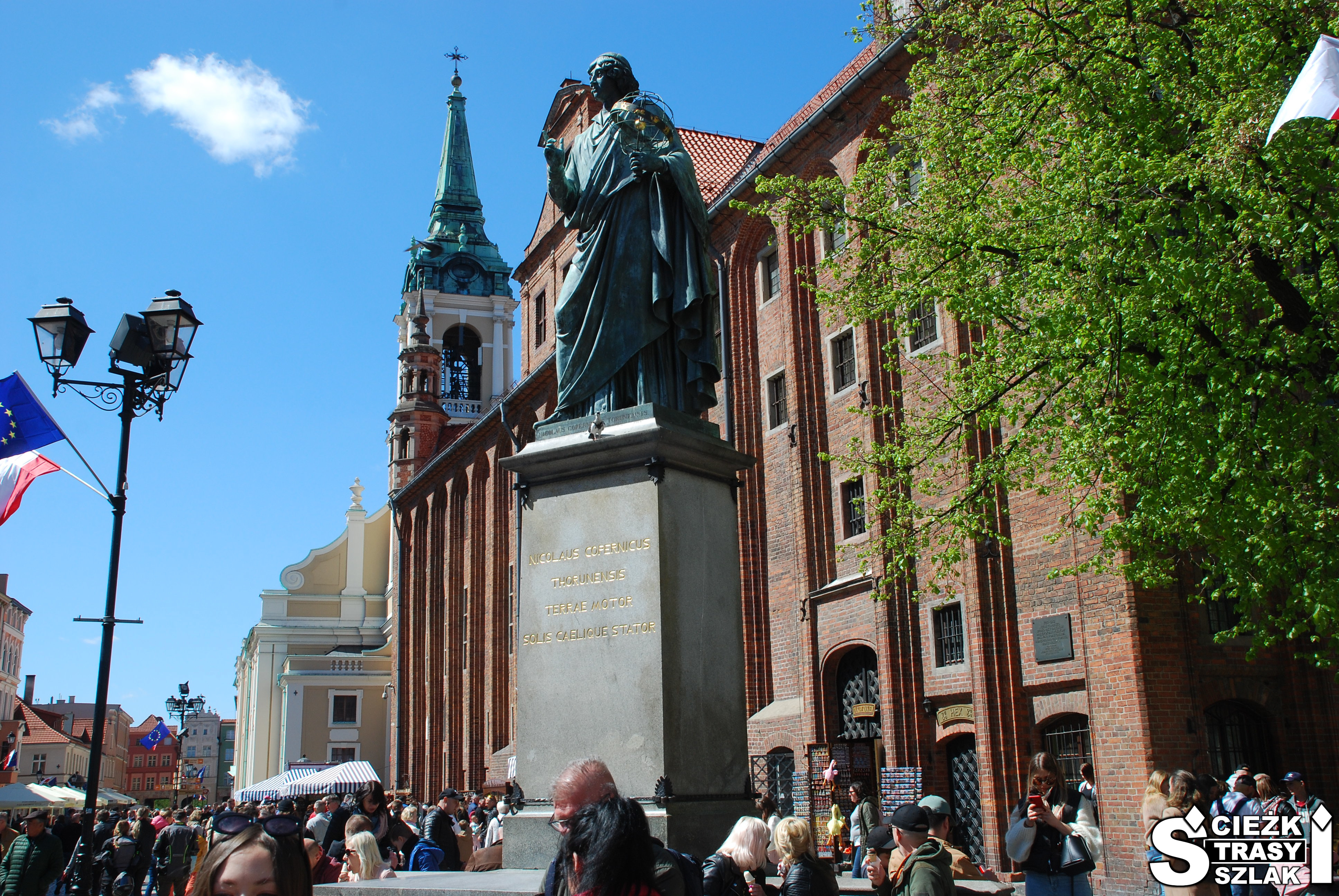 Pomnik Mikołaja Kopernika na Starówce miasta Toruń na wysokim postumencie przy zabytkowym kościele