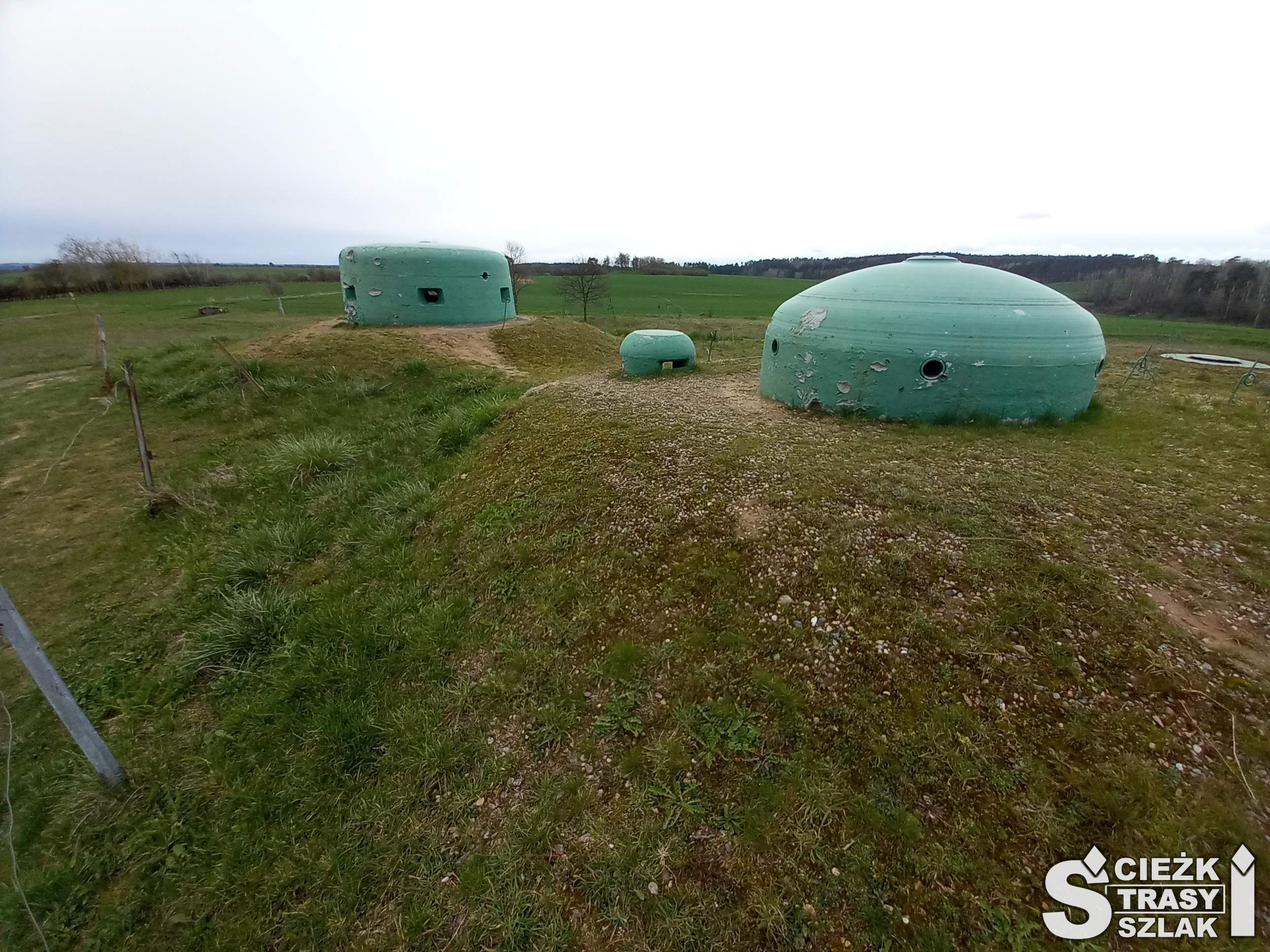 Trzy bunkry hitlerowskie w kształcie walca z otworami na broń i do obserwacji zagrożenia nad powierzchnią ziemi