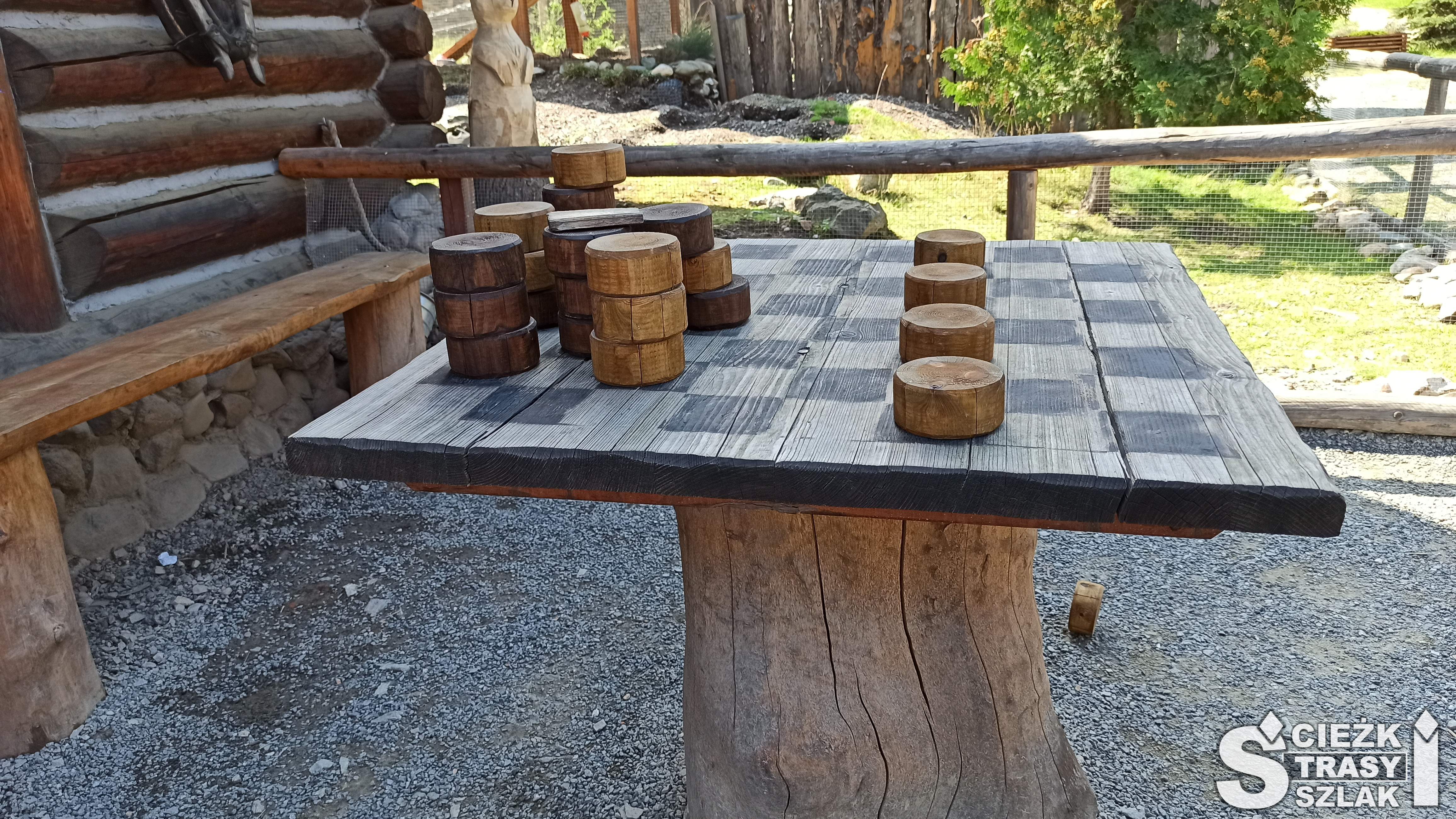 Drewniany stół z szachownicą do gry w warcaby dużymi drewnianymi pionkami przed wejściem do parku techniki