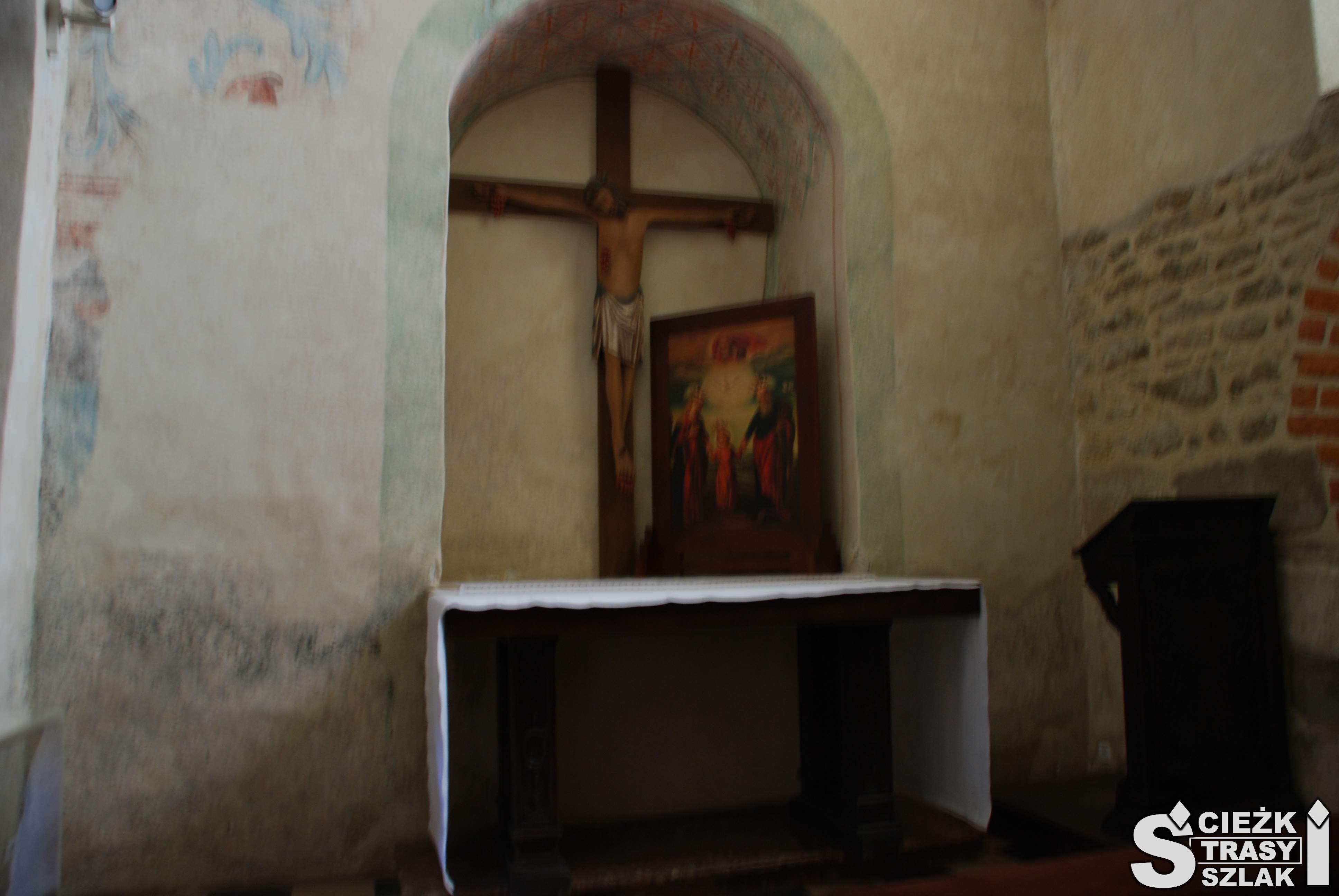 Łukowata wnęką z krzyżem na ołtarzyku przy ścianie wymagającej remontu we wnętrzu bazyliki w Miechowie