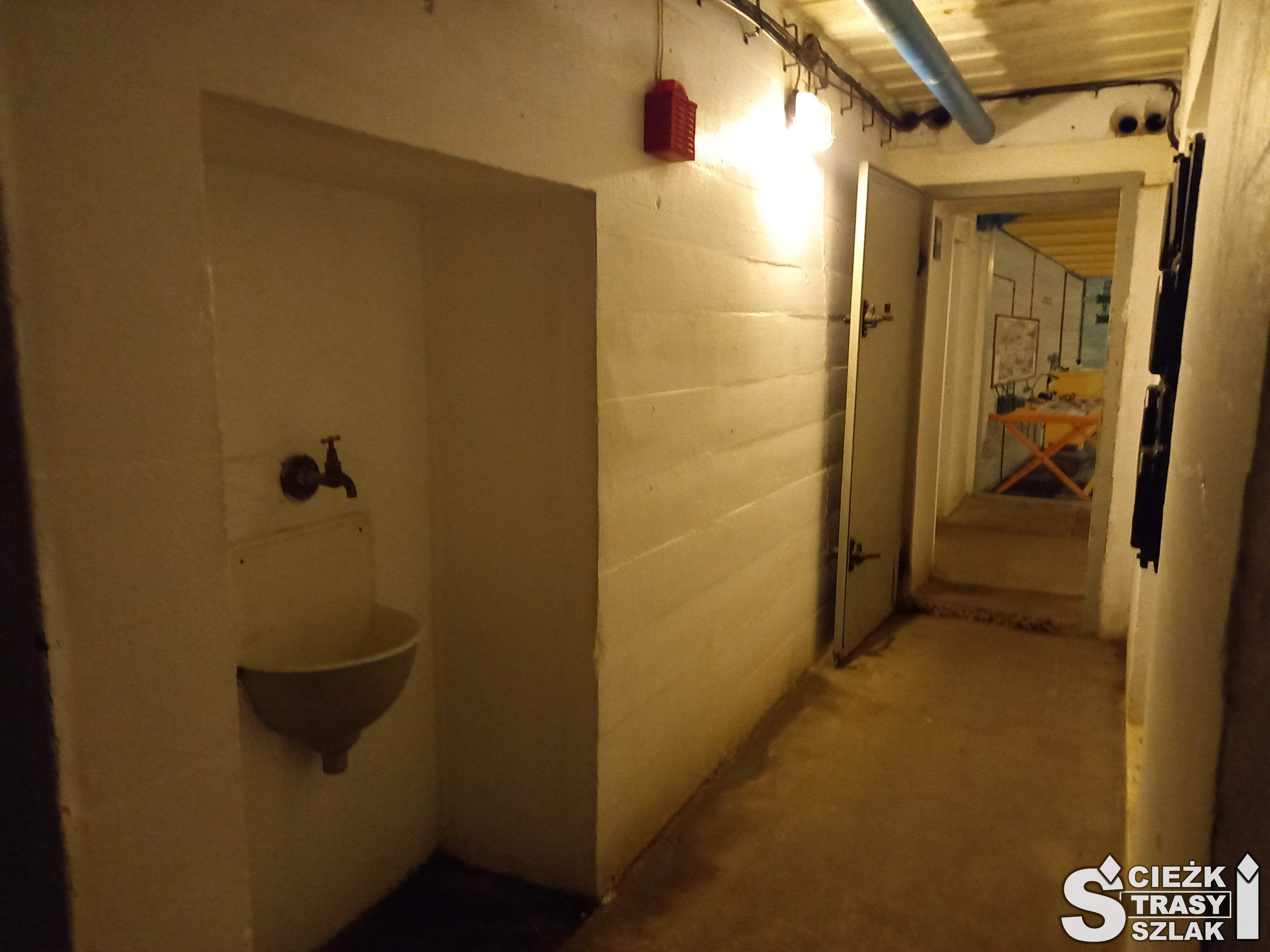 Długi wąski, oświetlony korytarz bunkrów w Międzyrzeczu i umywalka z kranem zawieszona na betonowej ścianie
