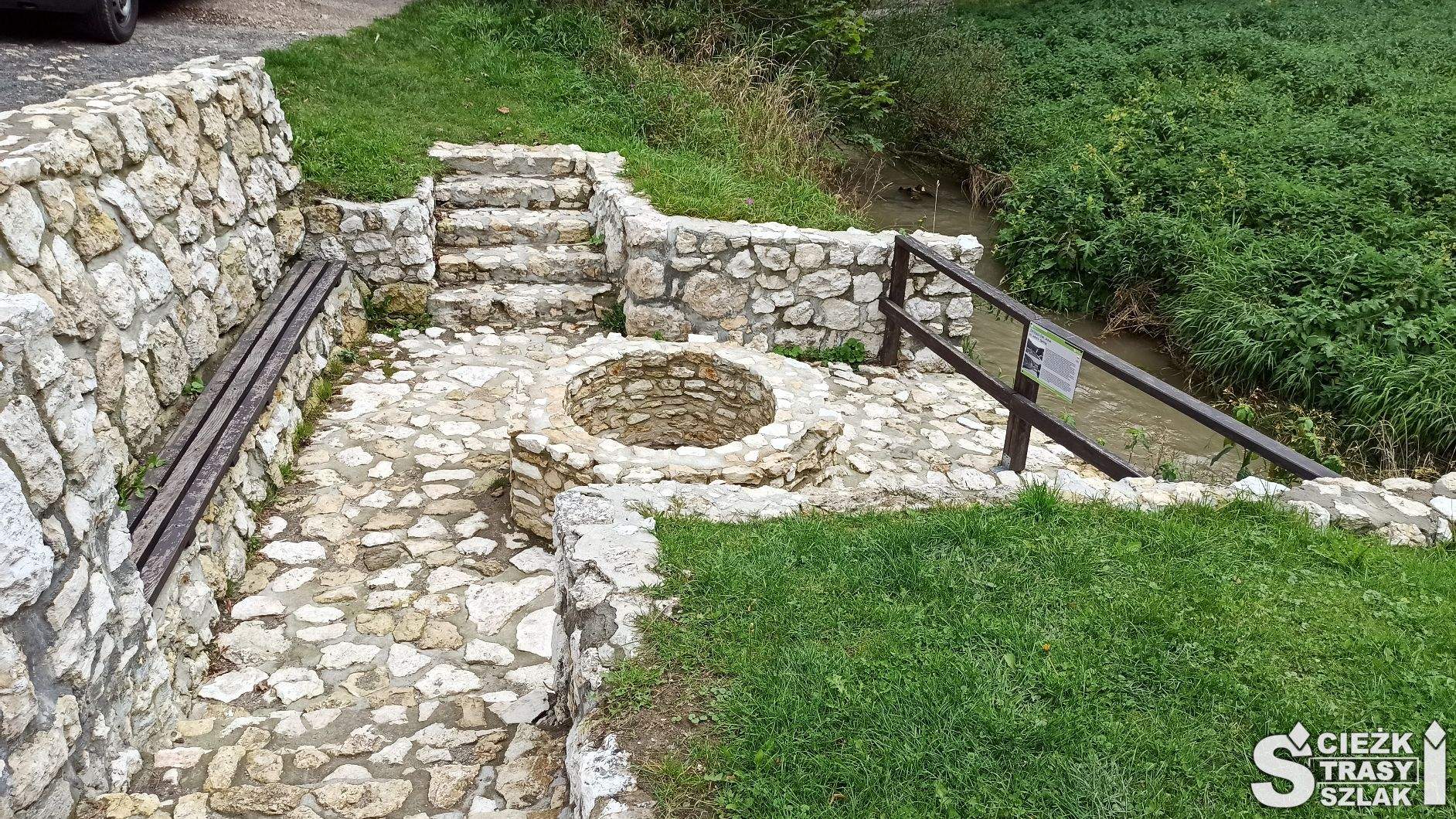 Ławka przy wyłożonej kamieniami ośmiobocznej studni ze źródlaną wodą przy rzece Prądnik
