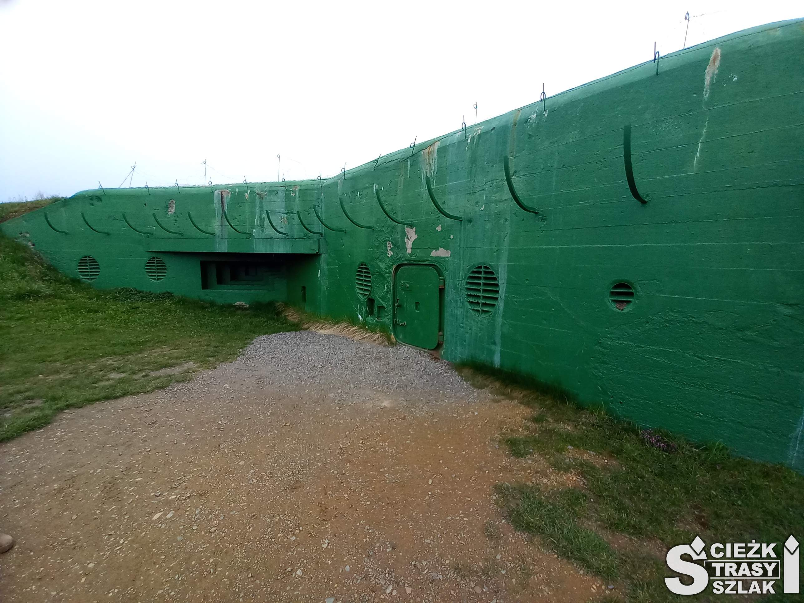 Betonowe wejście do bunkrów ukryte w skarpie z niewielkimi drzwiami i otworami wentylacyjnymi MRU Międzyrzecz