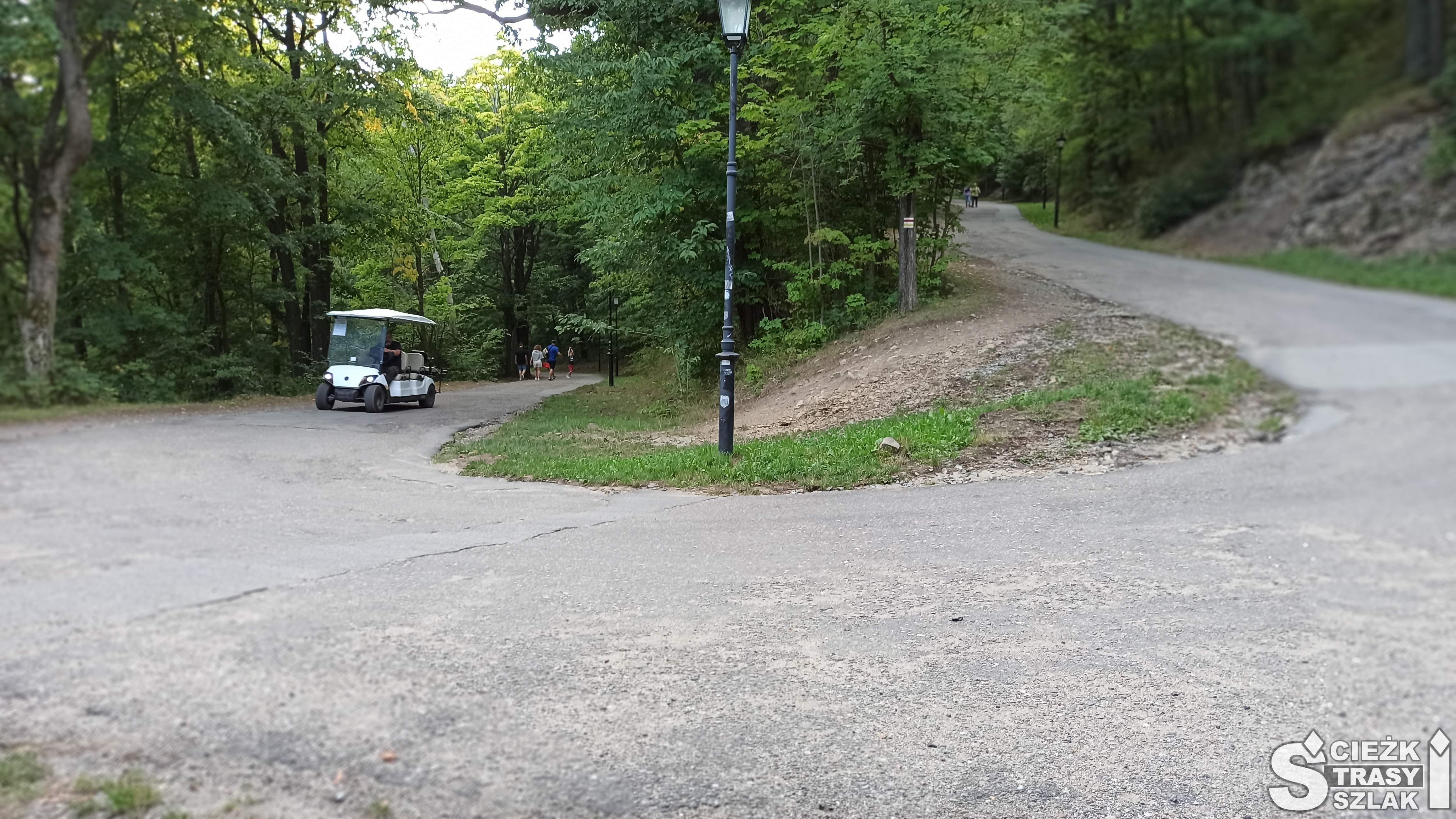 Elektryczny melex do przewozu turystów na ostrym zakręcie drogi asfaltowej z rebusami o Twierdzy Srebrna Góra