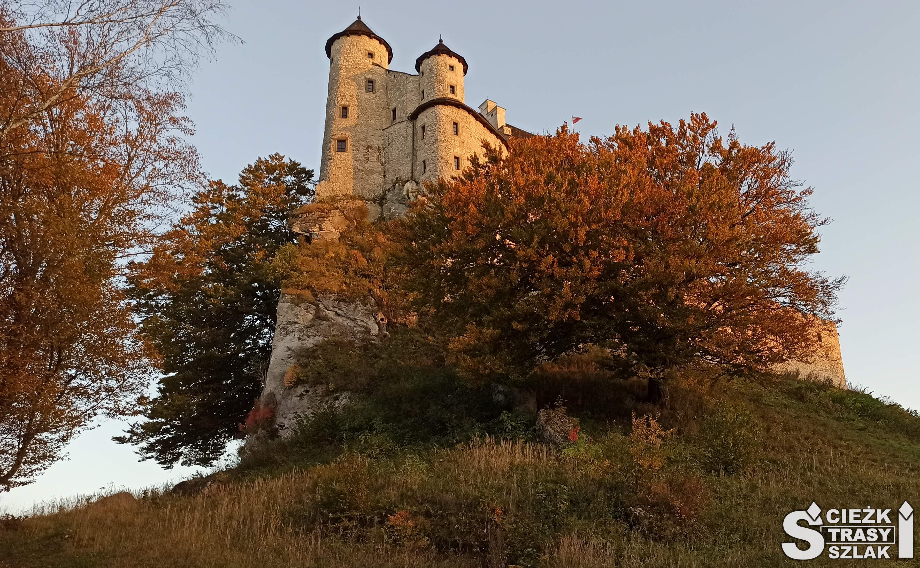 Dwie wieże Zamku na skale w Bobolicach otulone koronami drzew ubarwionych przez Polską Jesień