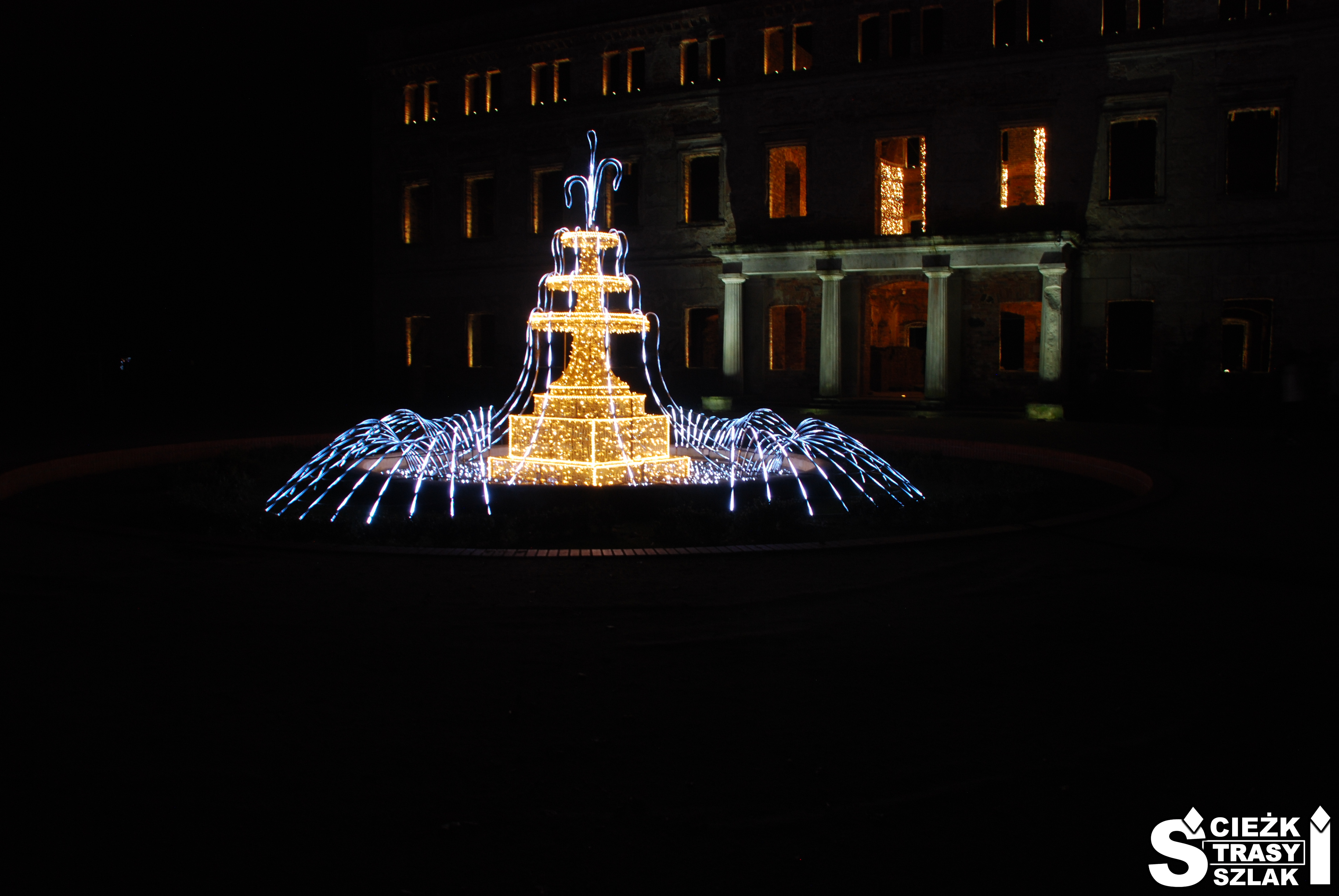 Podświetlona fontanna z imitującymi ruch wody efektami świetlnymi na tle podświetlonego Pałacu w Zatoniu