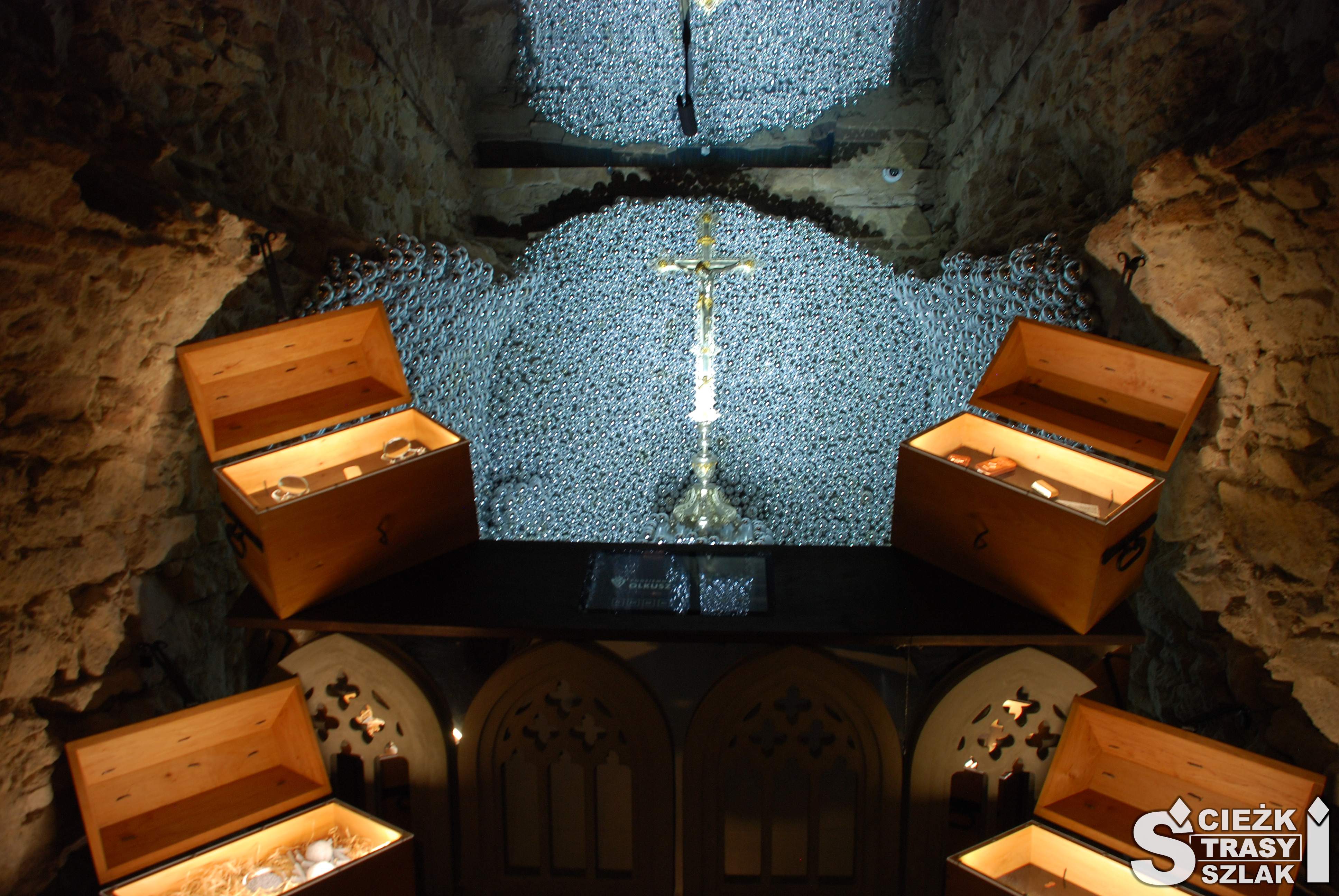 Srebrny Krzyż Gwarków Olkuskich na tle srebrnych kulek i skrzyń ze srebrem w podziemiach olkuskiego muzeum