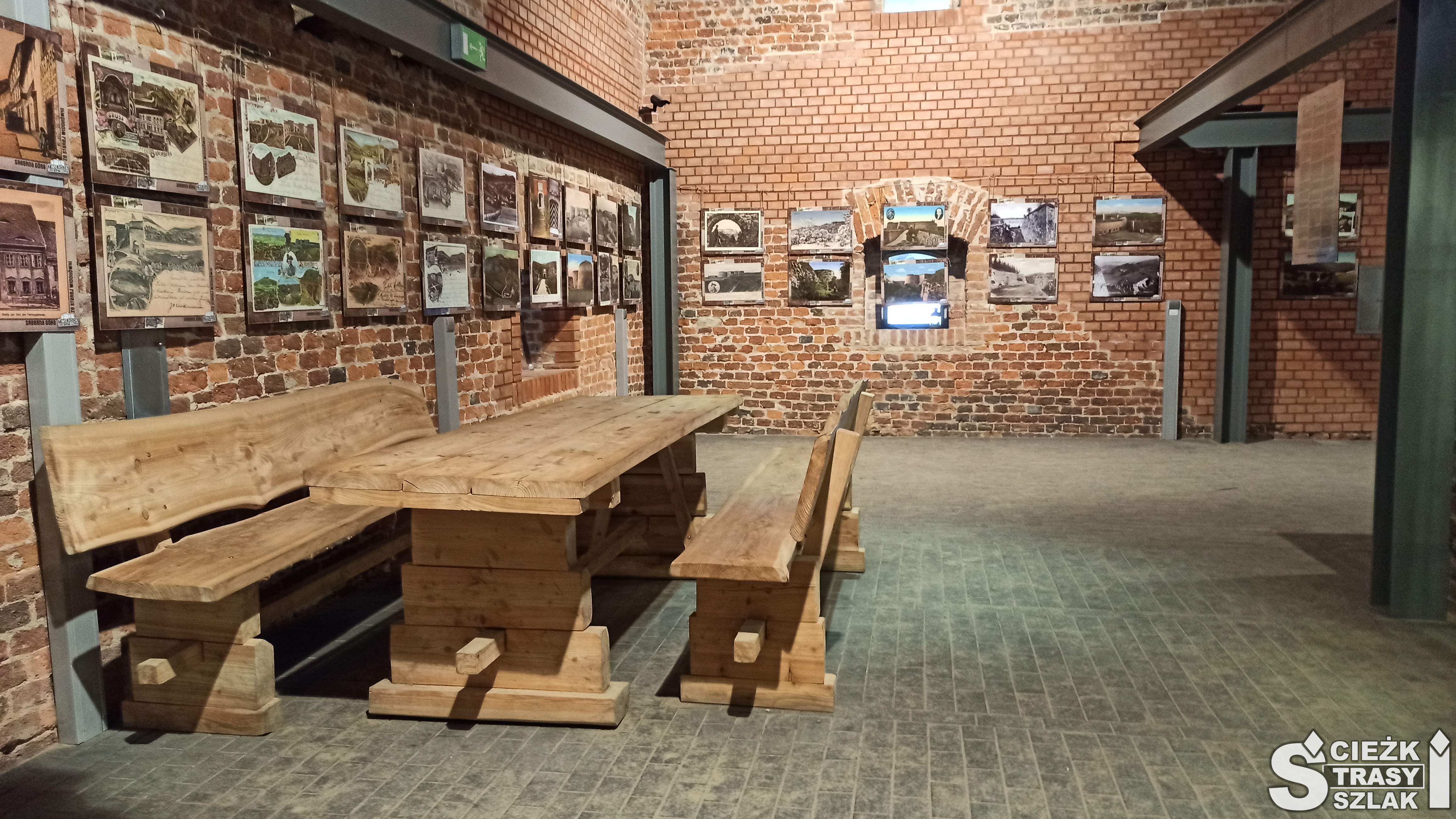 Ceglane ściany i  drewniany stół z ławkami ogrodowymi przy galerii o Twierdzy Srebrna Góra