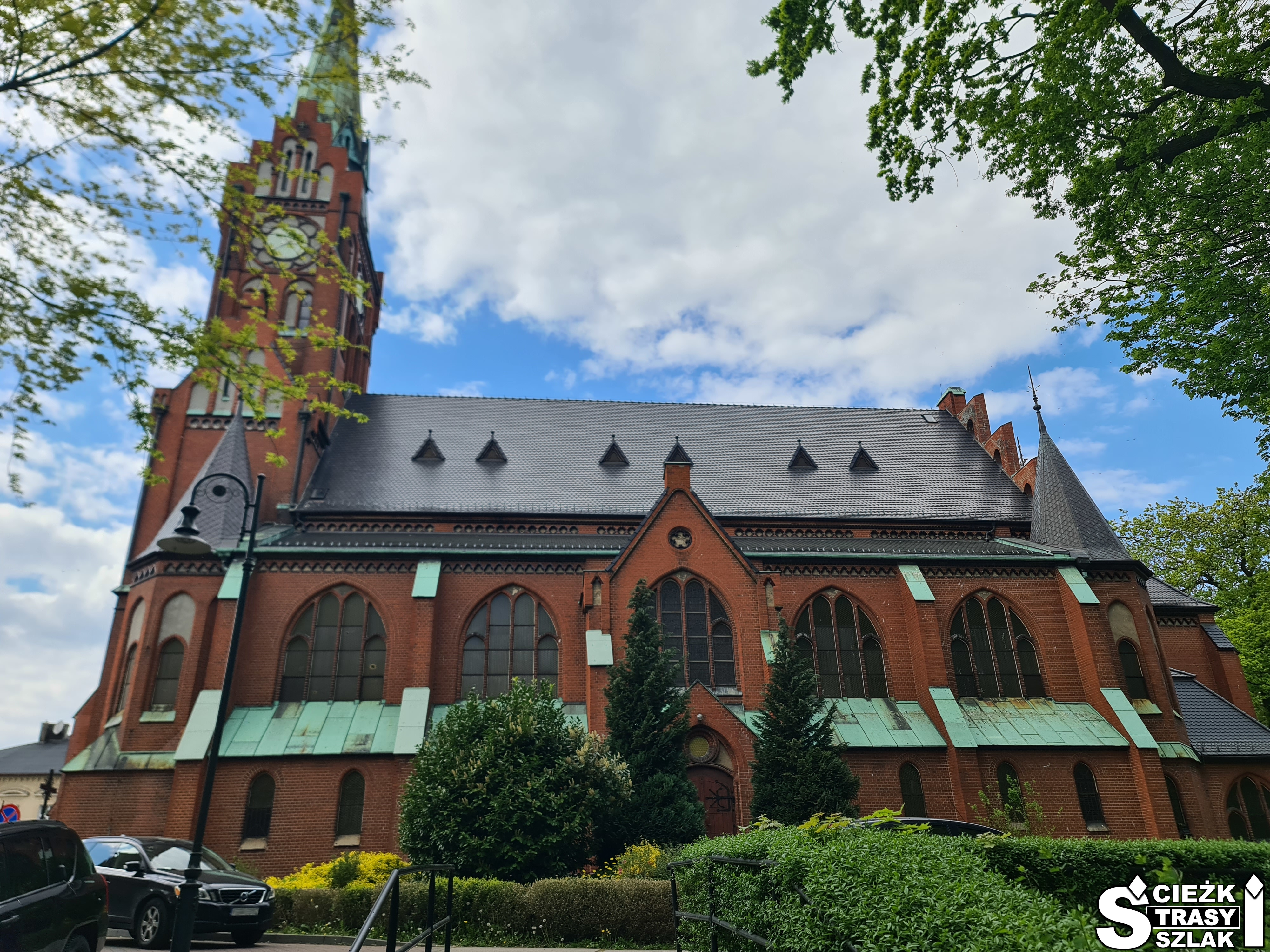 Kościół NMP Królowej Polski w Świebodzinie z cegły z wysoką wieżą i łukowatymi oknami przy parku miejskim